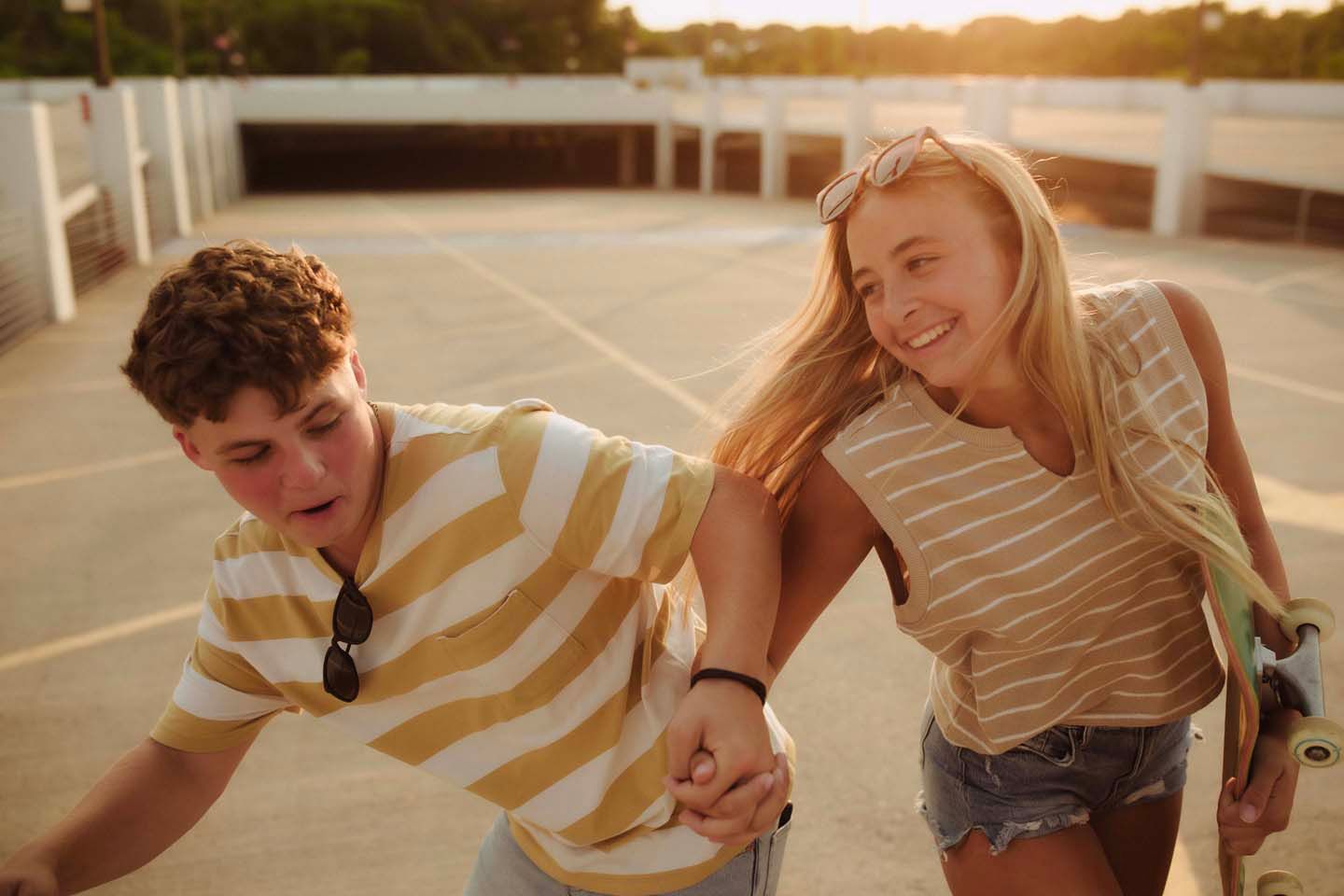 Happy teenage couple holding hands and laughing on a sunny rooftop skatepark.