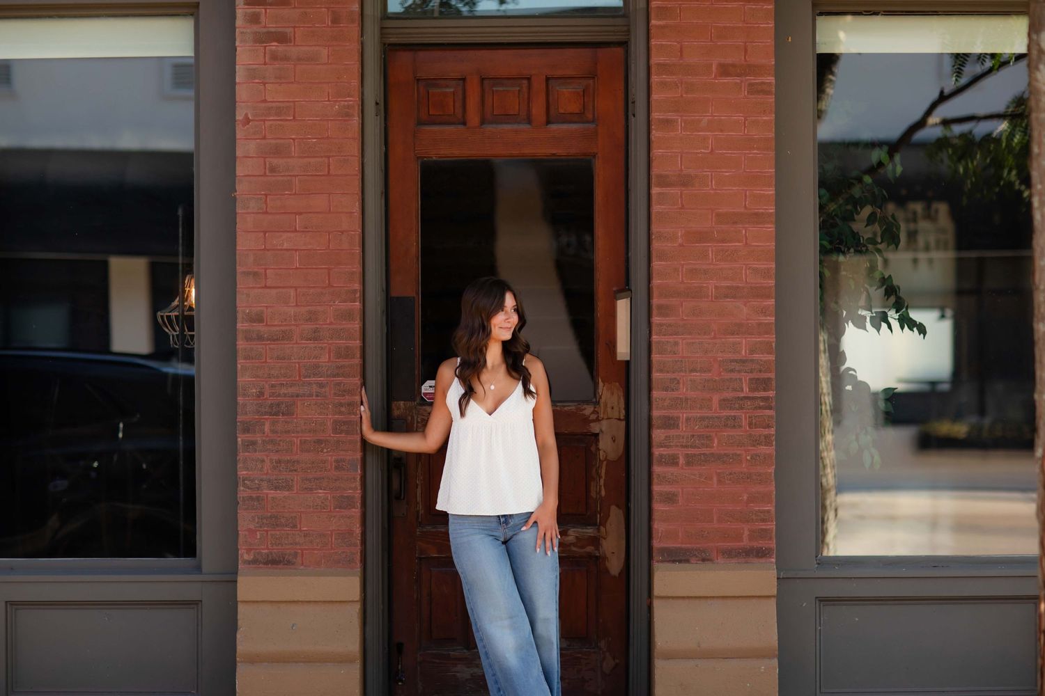 Woman in white top and jeans standing in a brick building doorway.