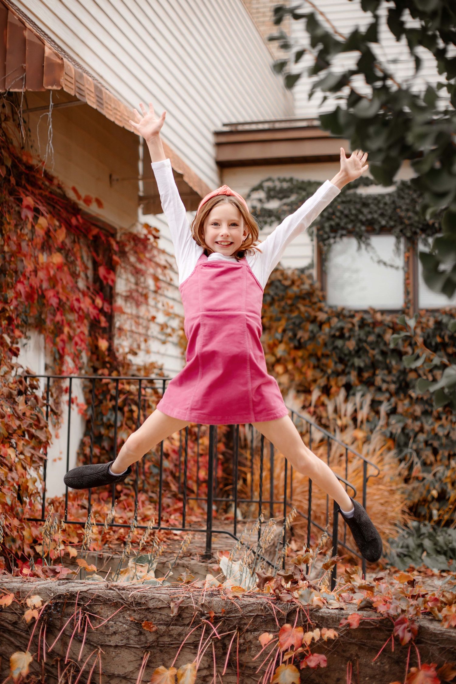Action shot of jumping figure in pink dress against autumn ivy covered wall.