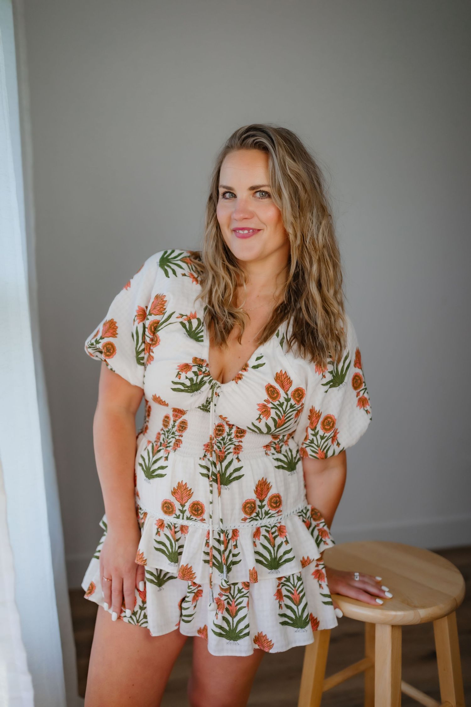 Floral white mini dress with orange flower pattern and short sleeves in indoor portrait setting.