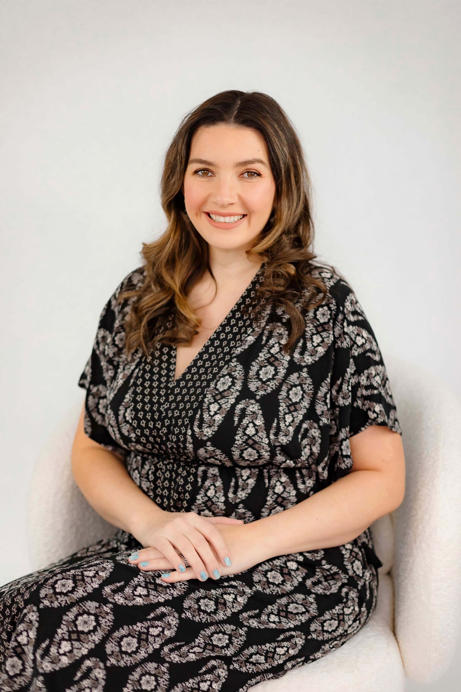 Seated portrait in black and white patterned wrap dress against white background.