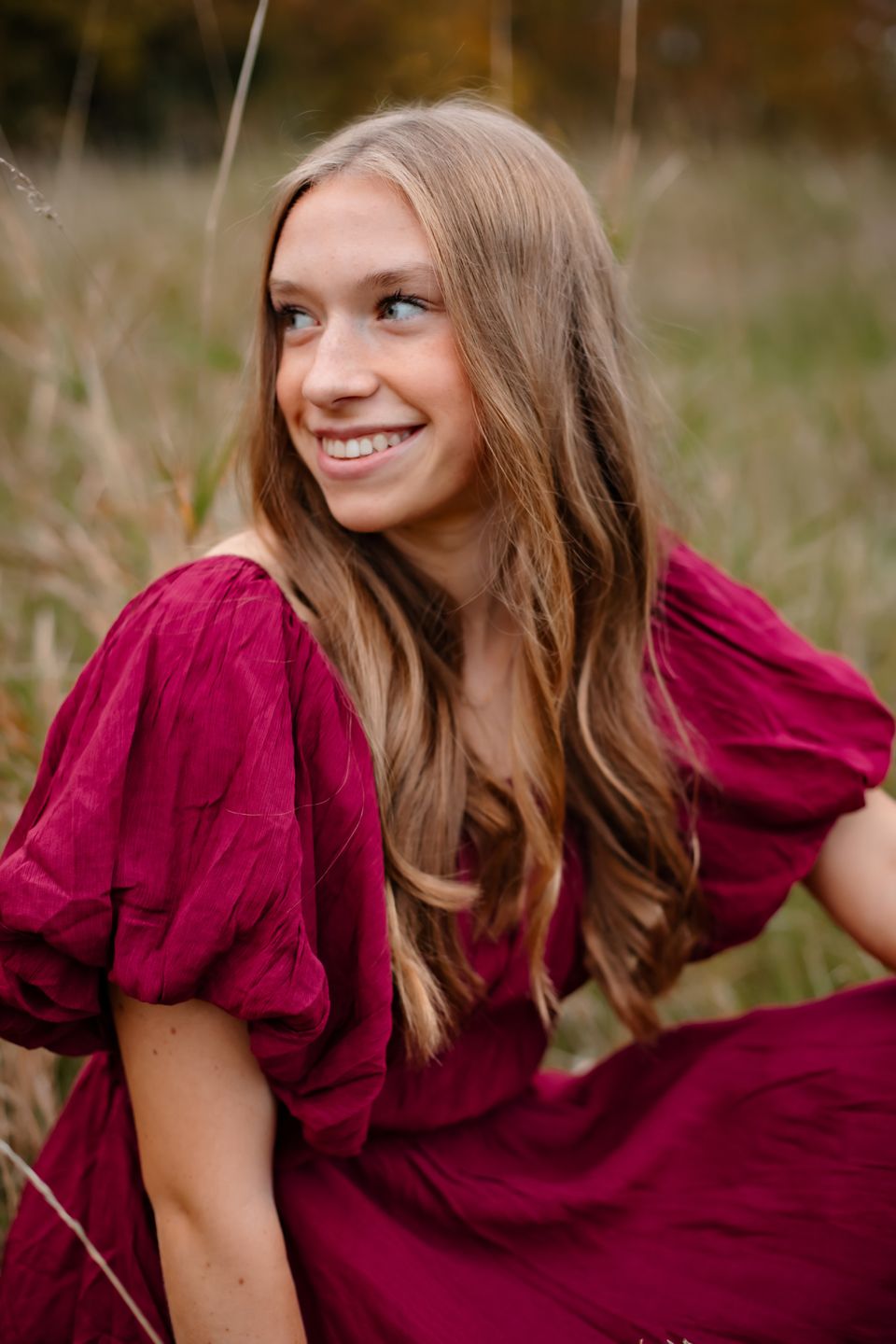 Close-up portrait in a burgundy dress with warm autumn lighting in a natural outdoor setting.