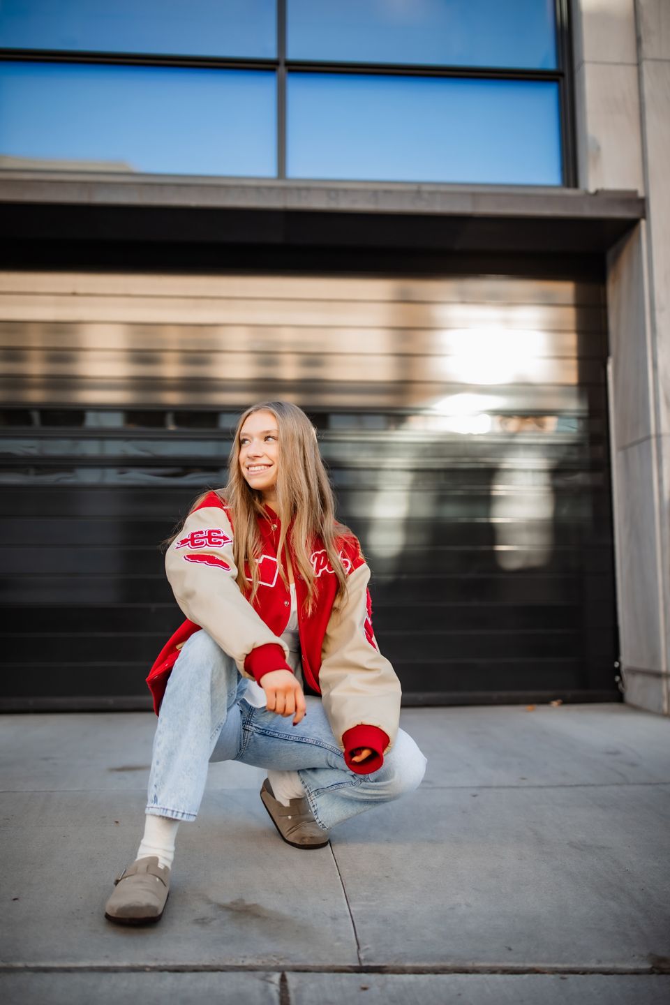 Candid outdoor portrait wearing varsity jacket and light denim in urban setting.