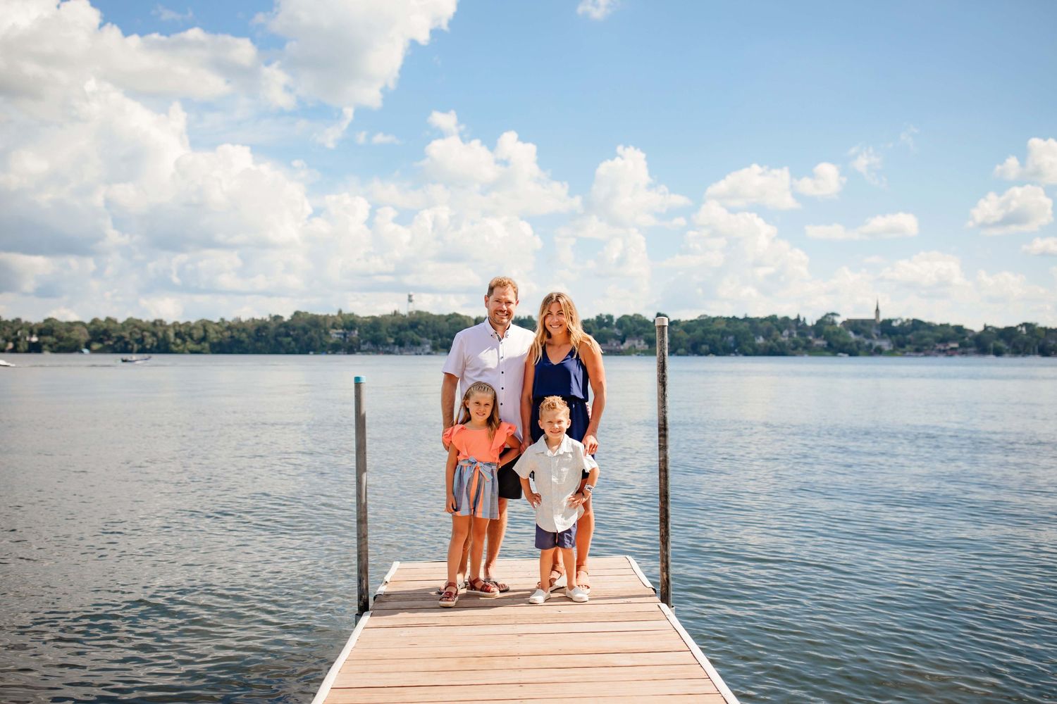 Family standing together on wooden dock over peaceful lake on sunny day.