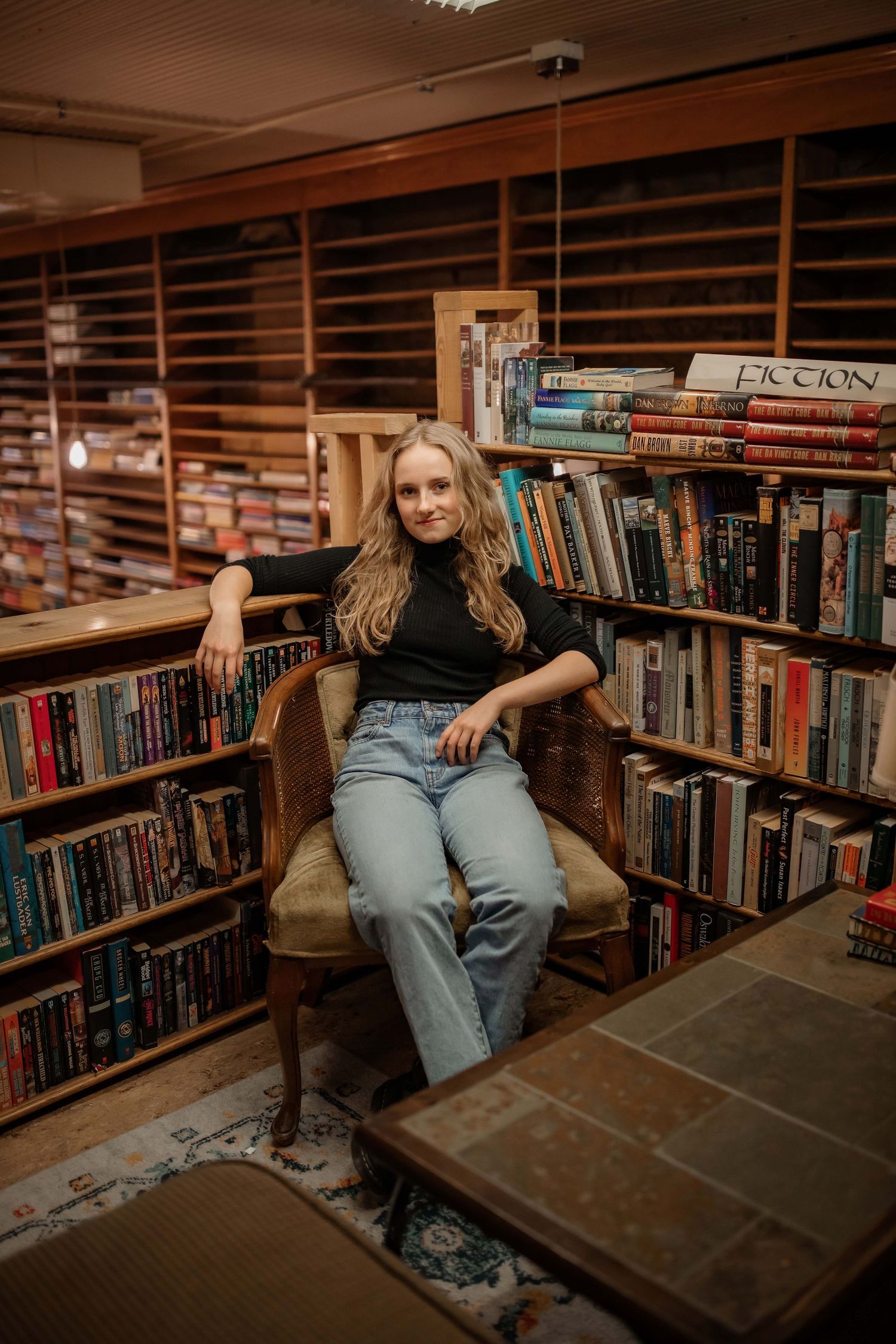 Casual portrait in library setting surrounded by wooden bookshelves.