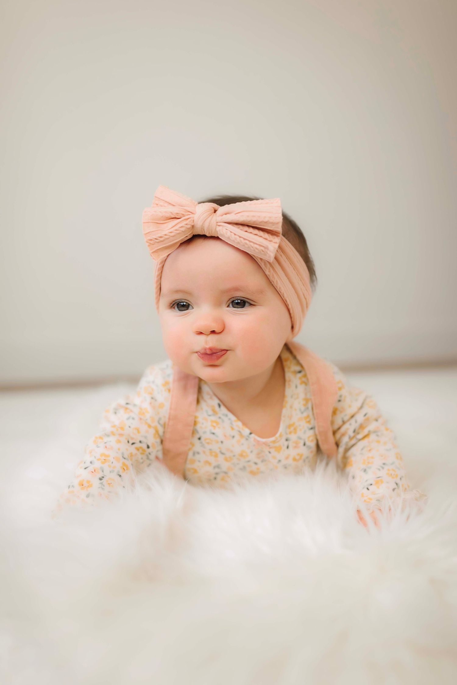 Baby in peach headband and floral outfit making playful expression.