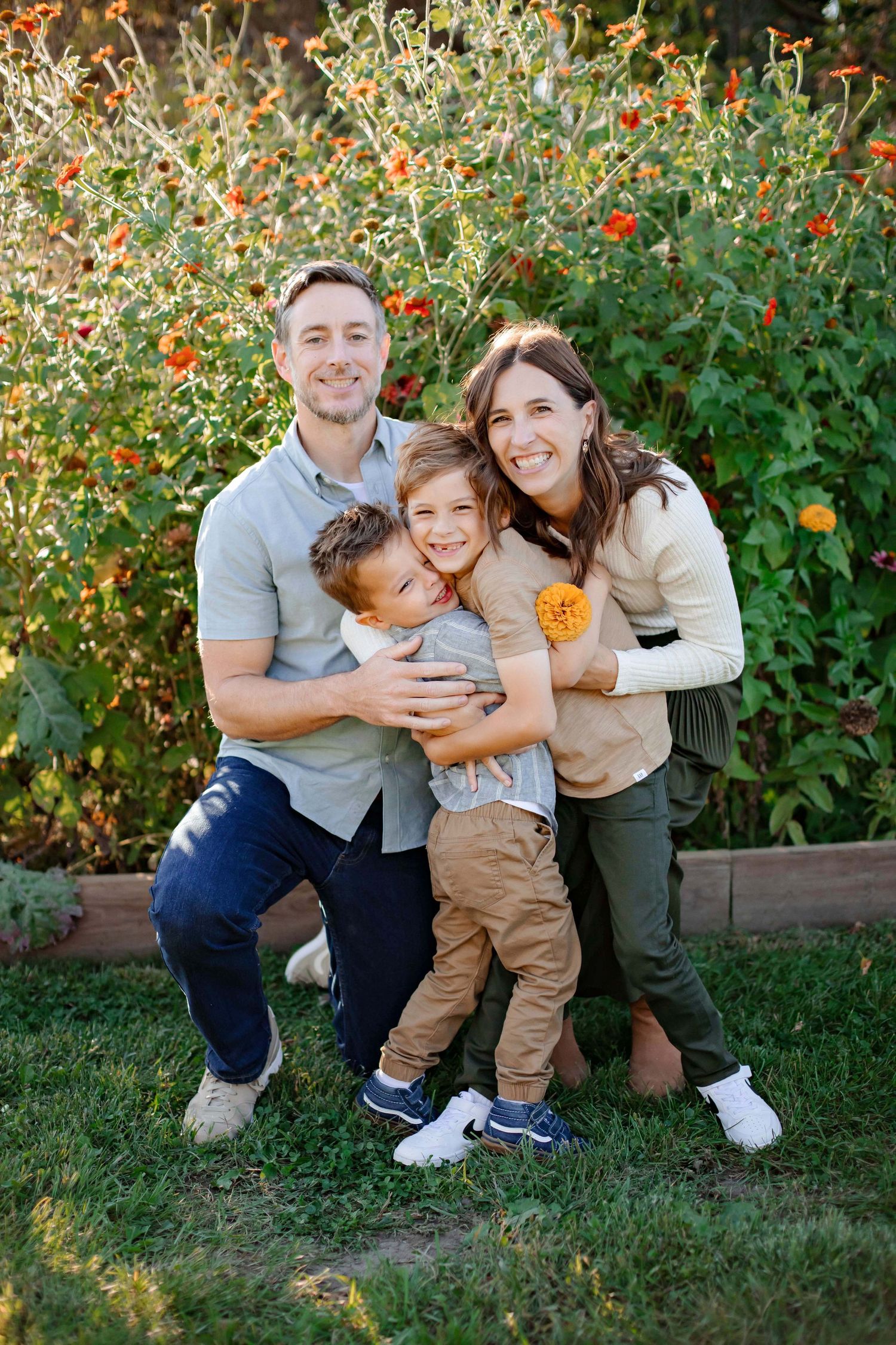 Family poses together in front of blooming orange flowers in garden setting.