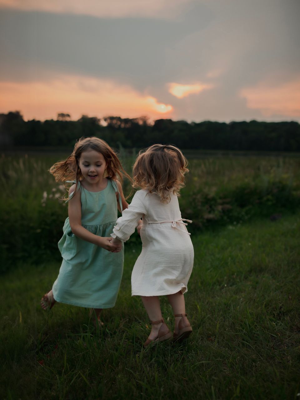 Two people in casual dresses dance together in a field during sunset.