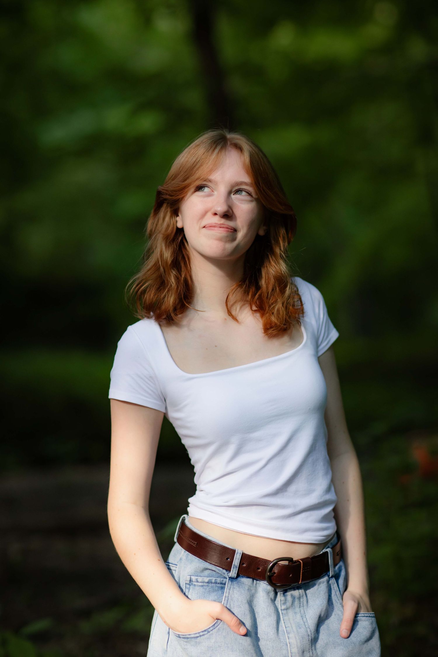 A figure in a white crop top and high-waisted jeans poses outdoors against a blurred green background.