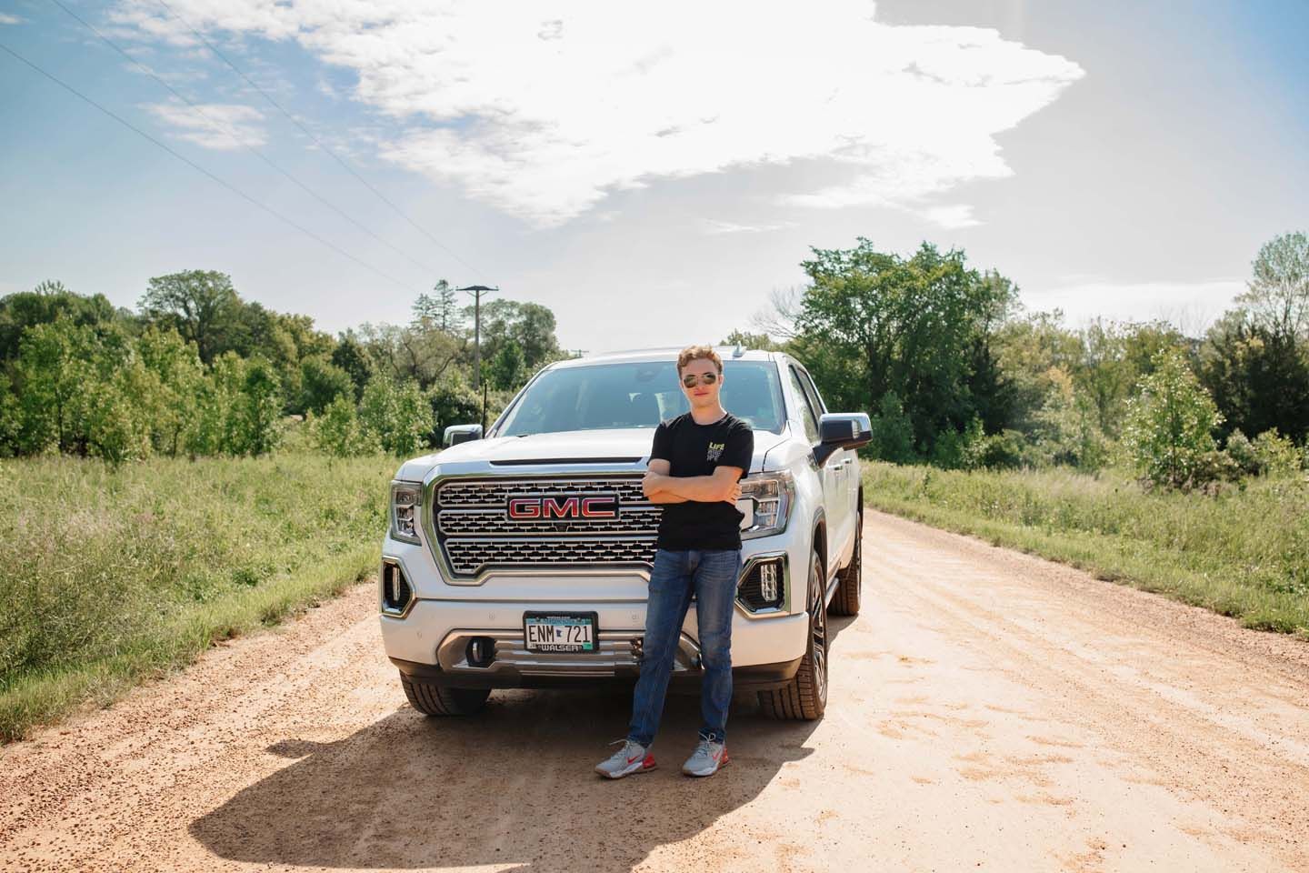 Person standing next to white GMC truck on dirt road in rural setting.