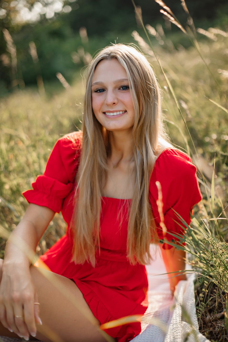 Person in a red dress sitting in tall golden grass during sunset.