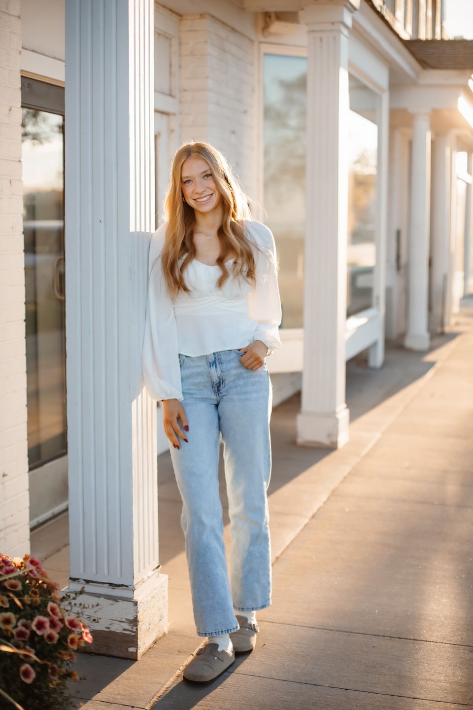 Casual street style portrait with light sweater and jeans against white colonial storefront columns.