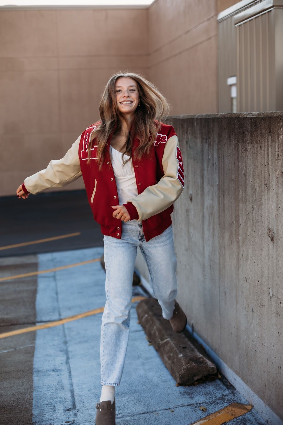 Dynamic lifestyle portrait in varsity jacket and jeans against urban backdrop.