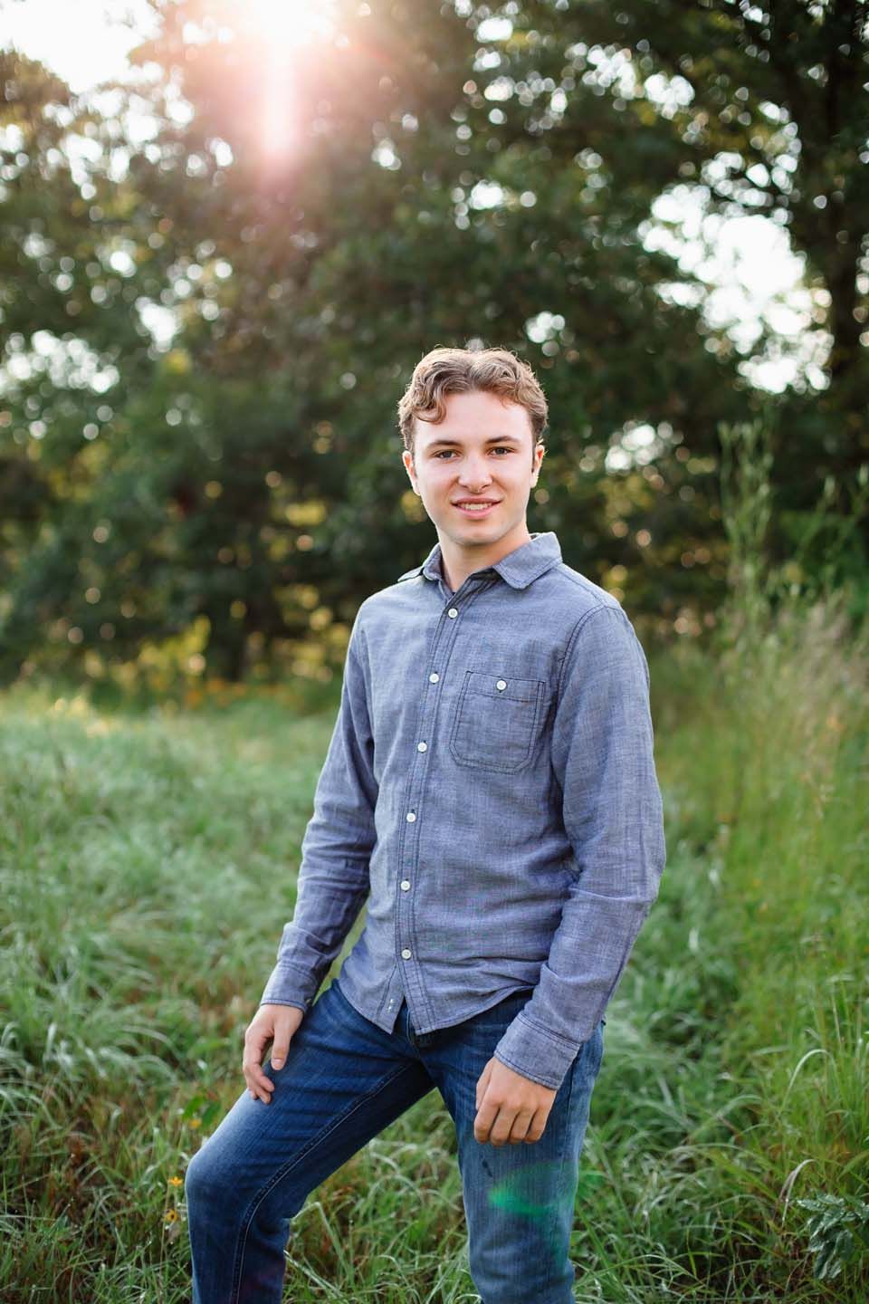Outdoor portrait with sun flare through trees showing person in chambray button-down shirt.