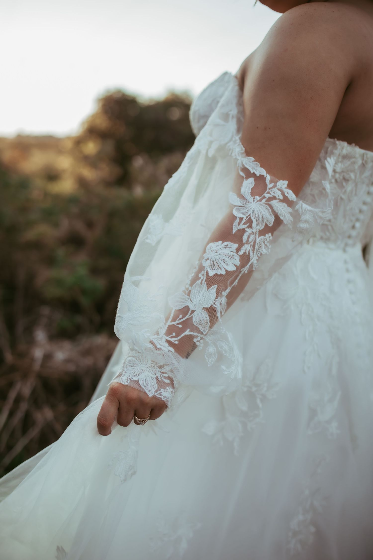 Detail shot of white lace floral applique on sheer wedding dress sleeve.