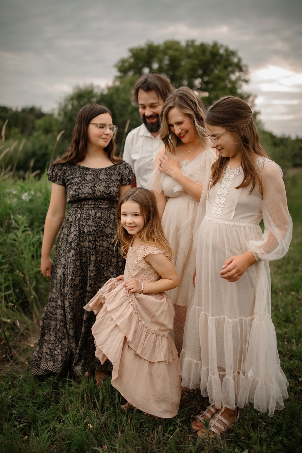 Family wearing coordinated dresses poses together in meadow at sunset.