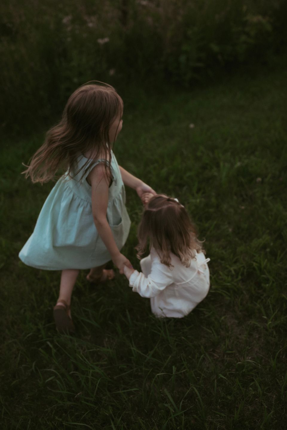 Two people in summer dresses hold hands while playing in a grassy field.