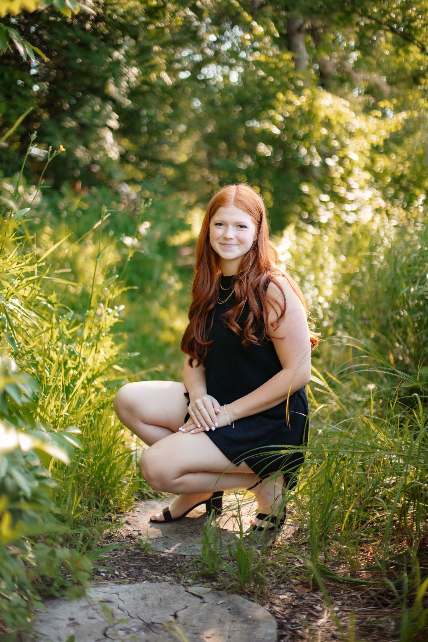 Outdoor portrait in lush garden setting with black dress among greenery and sunlit foliage.