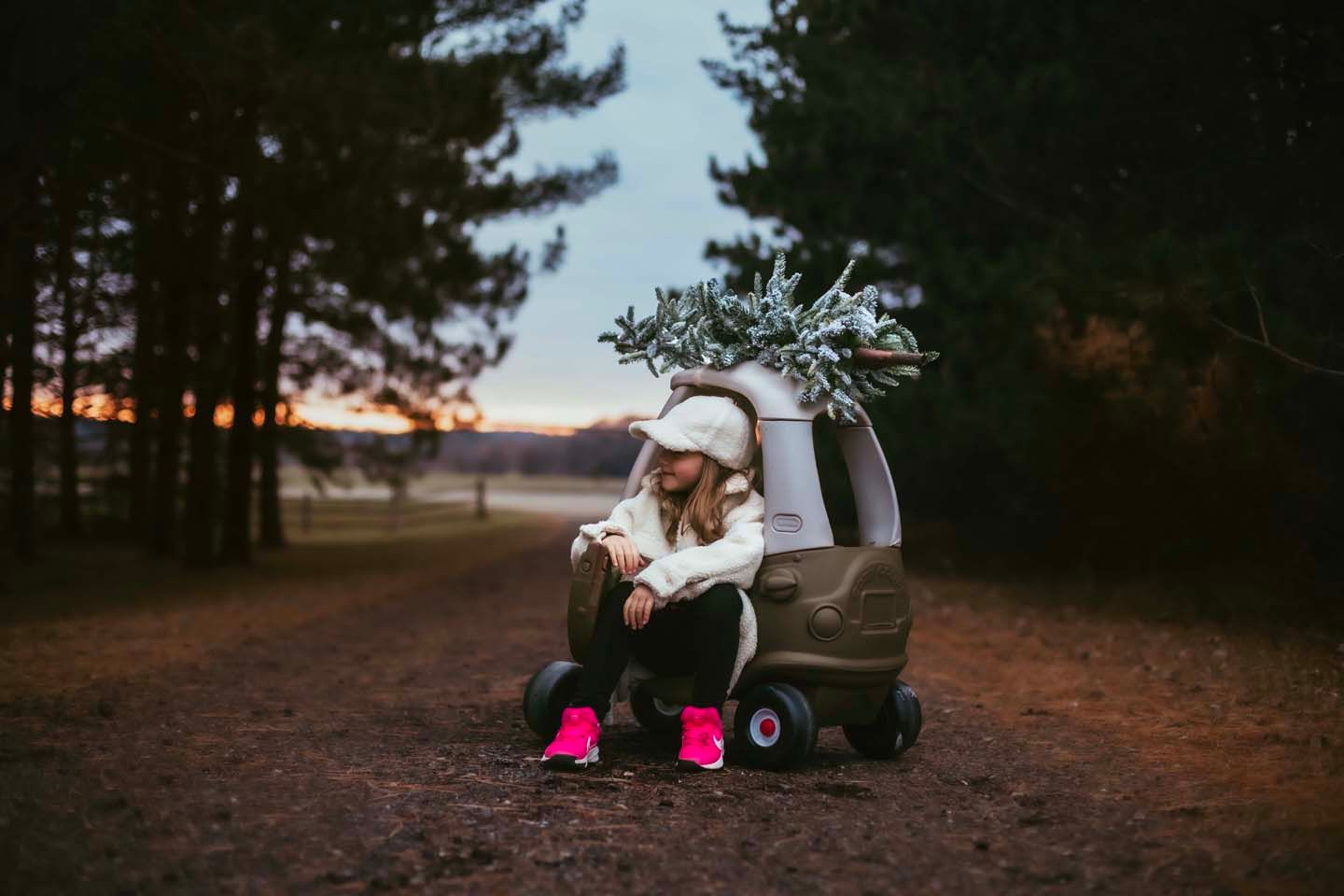 Child sitting in toy car at dusk in forest setting.
