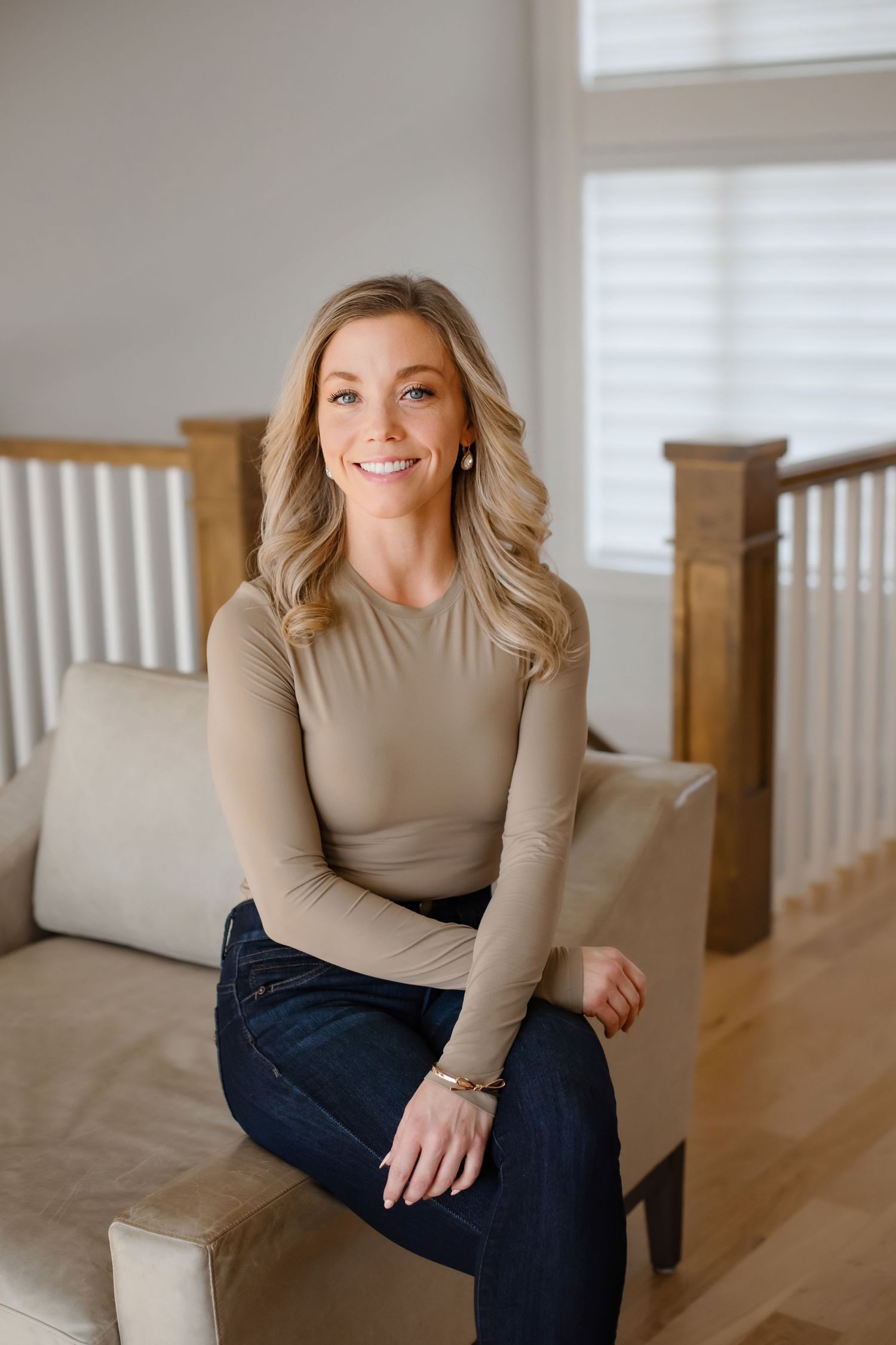 Casual indoor portrait of someone sitting on a beige couch wearing a tan sweater and dark jeans.