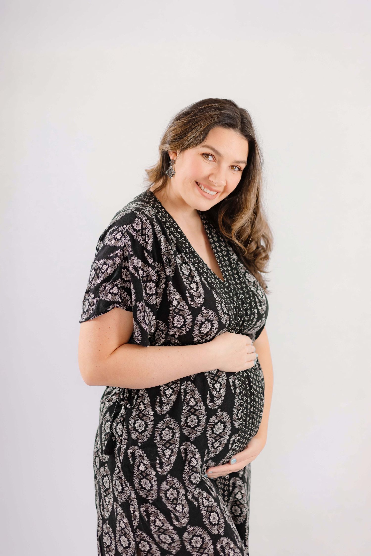 Expectant mother poses in black and white patterned wrap dress against light background.