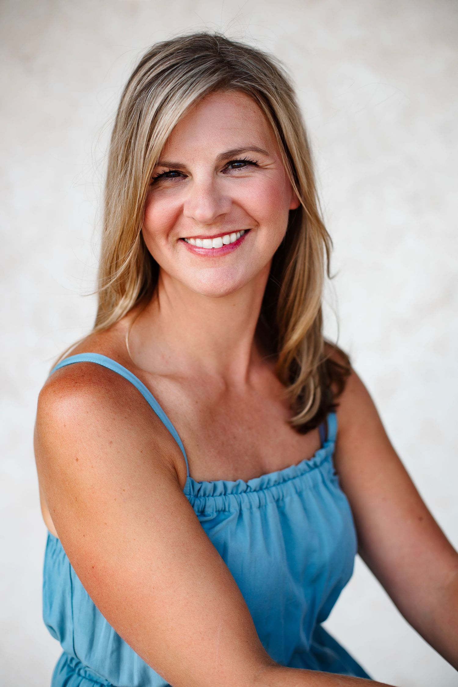 Professional portrait of a bright smile against a neutral background wearing a light blue summer dress.