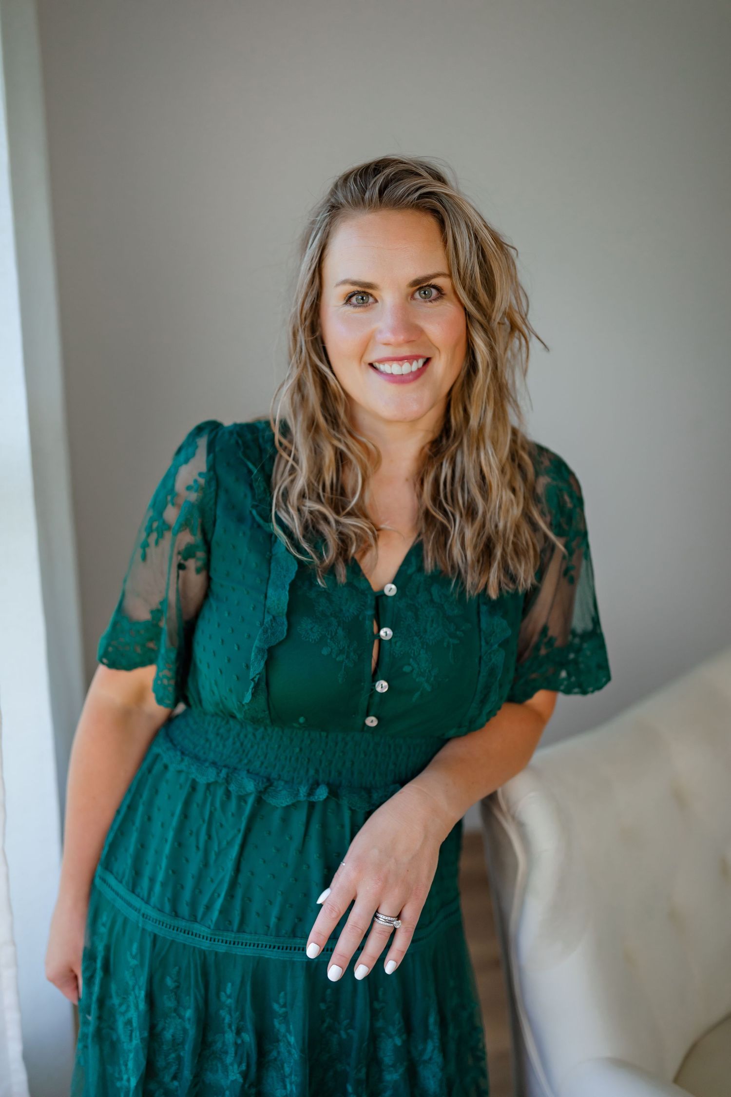 Deep green lace dress with sheer sleeves photographed against light gray wall.