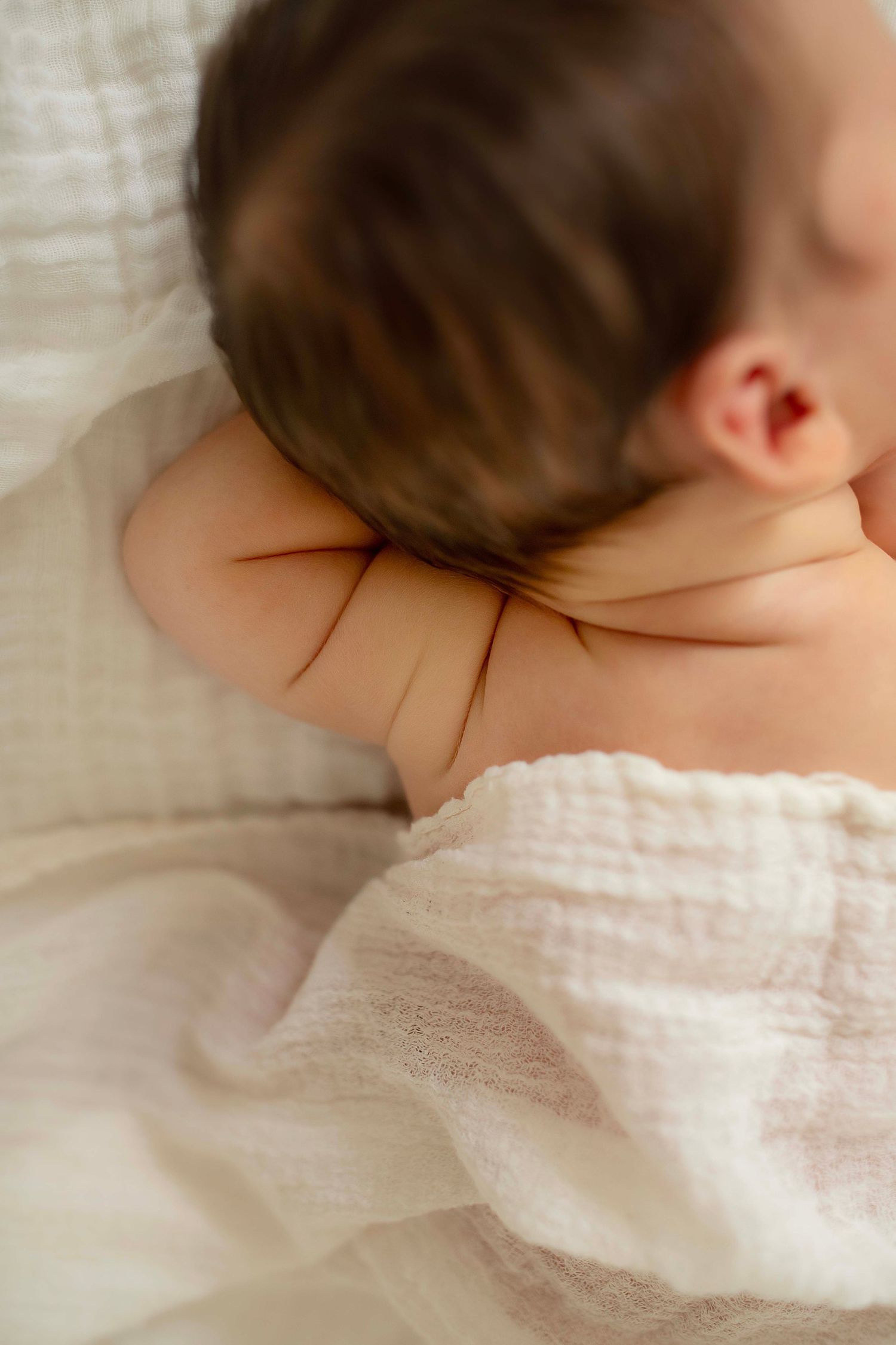 Sleeping newborn baby with dark hair wrapped in a soft white muslin cloth.