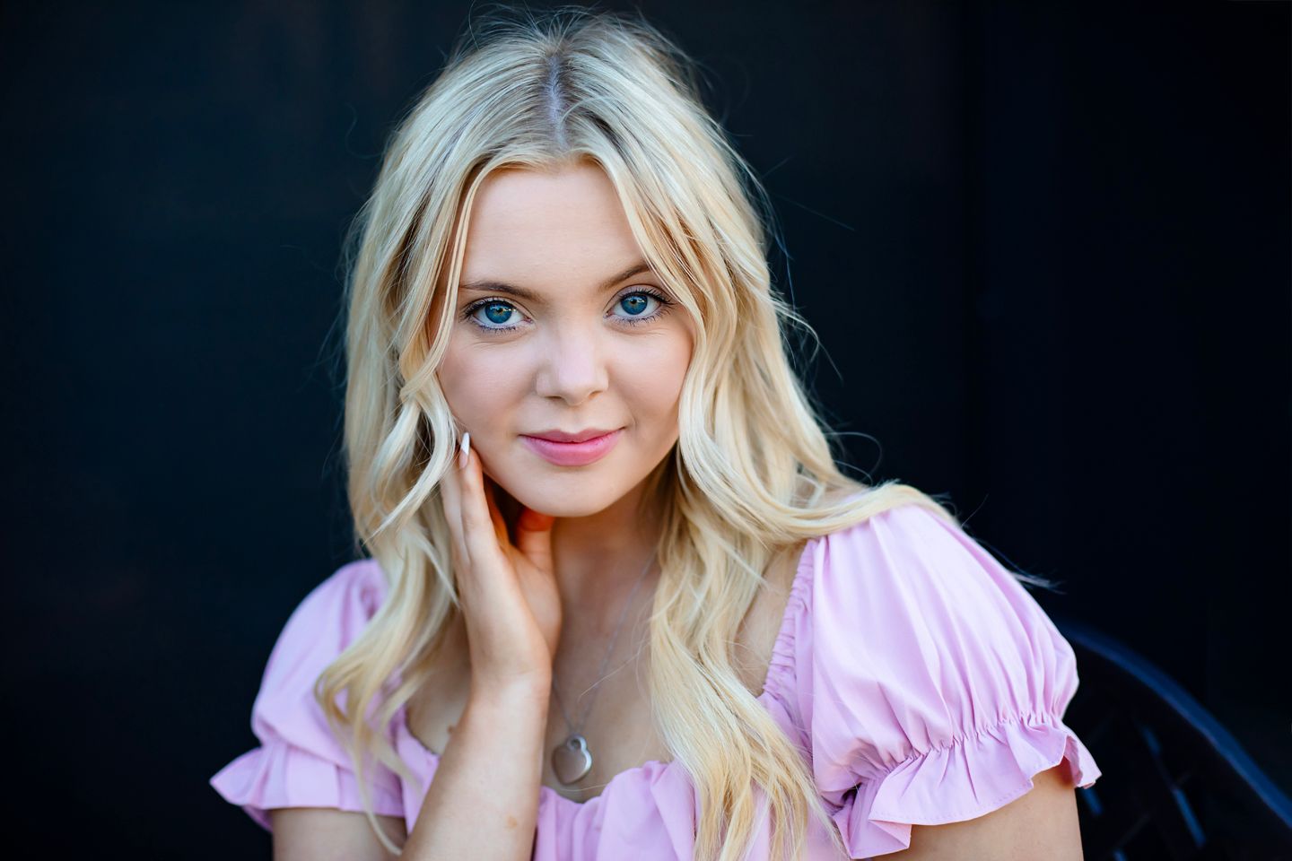 Close-up portrait wearing a pink puff sleeve top against a dark background.