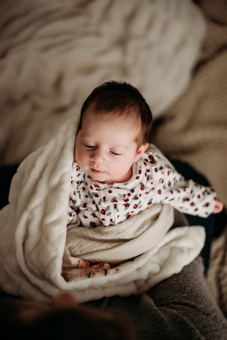 Sleeping infant wearing floral print outfit nestled in cream colored blankets.