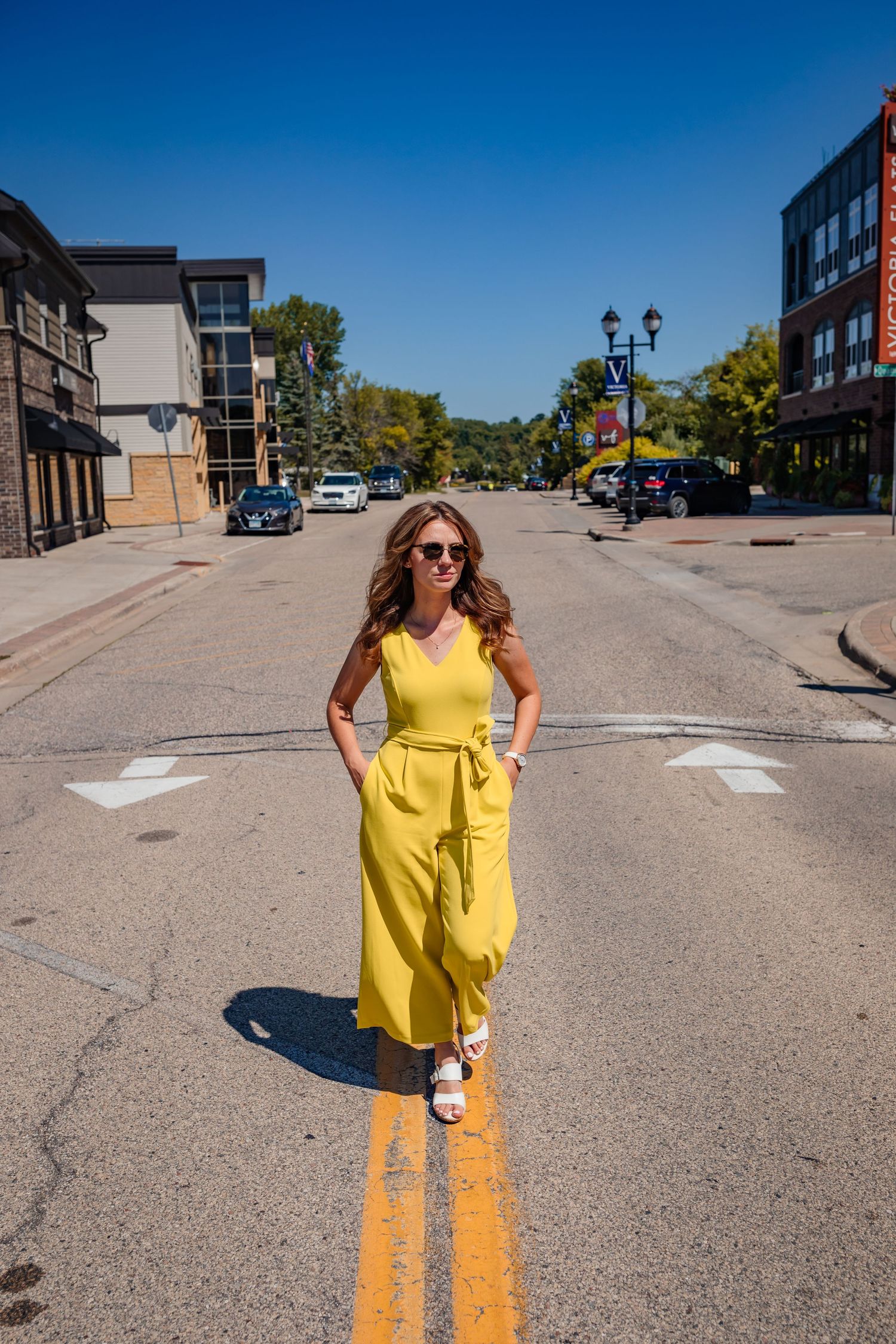 Woman in yellow dress poses confidently on double yellow lines of empty street.