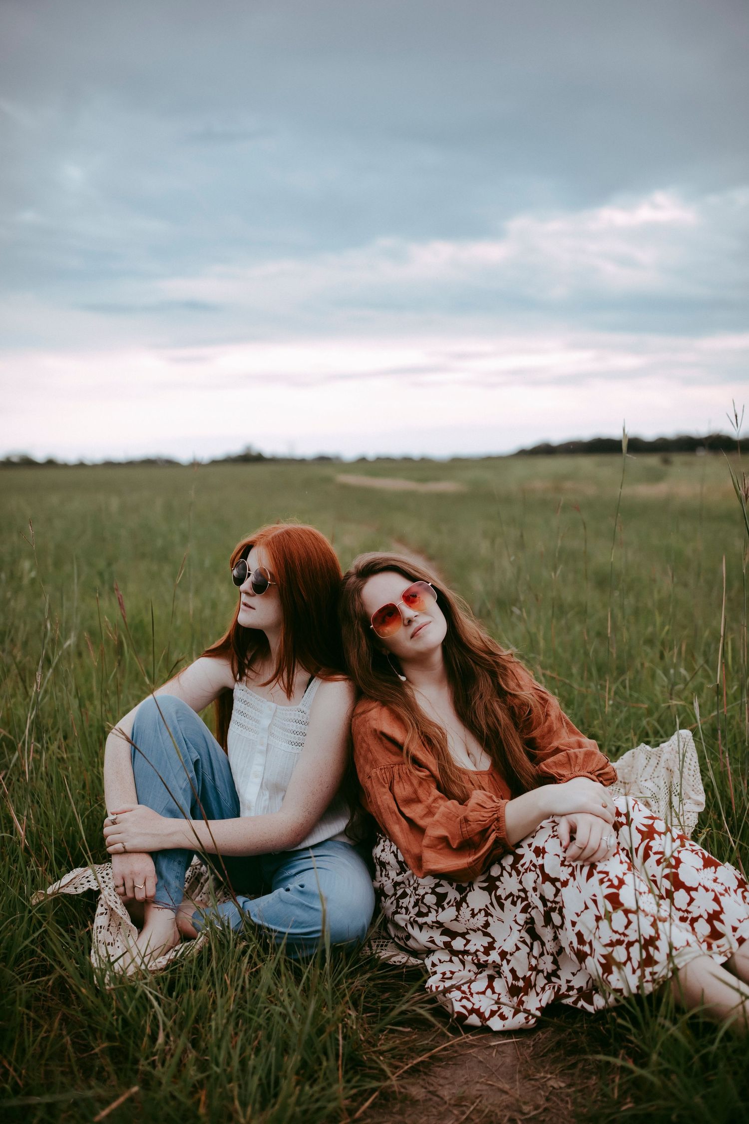 Friends in contrasting outfits relax together in a grassy field under moody skies.