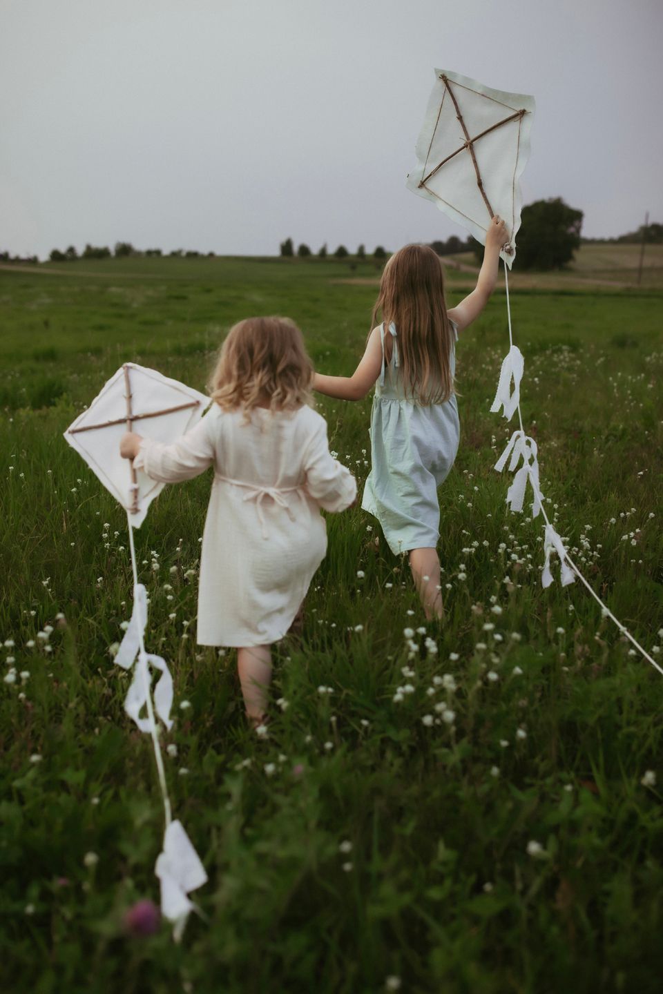 Two children holding homemade kites with streamers while standing in a flowering meadow.