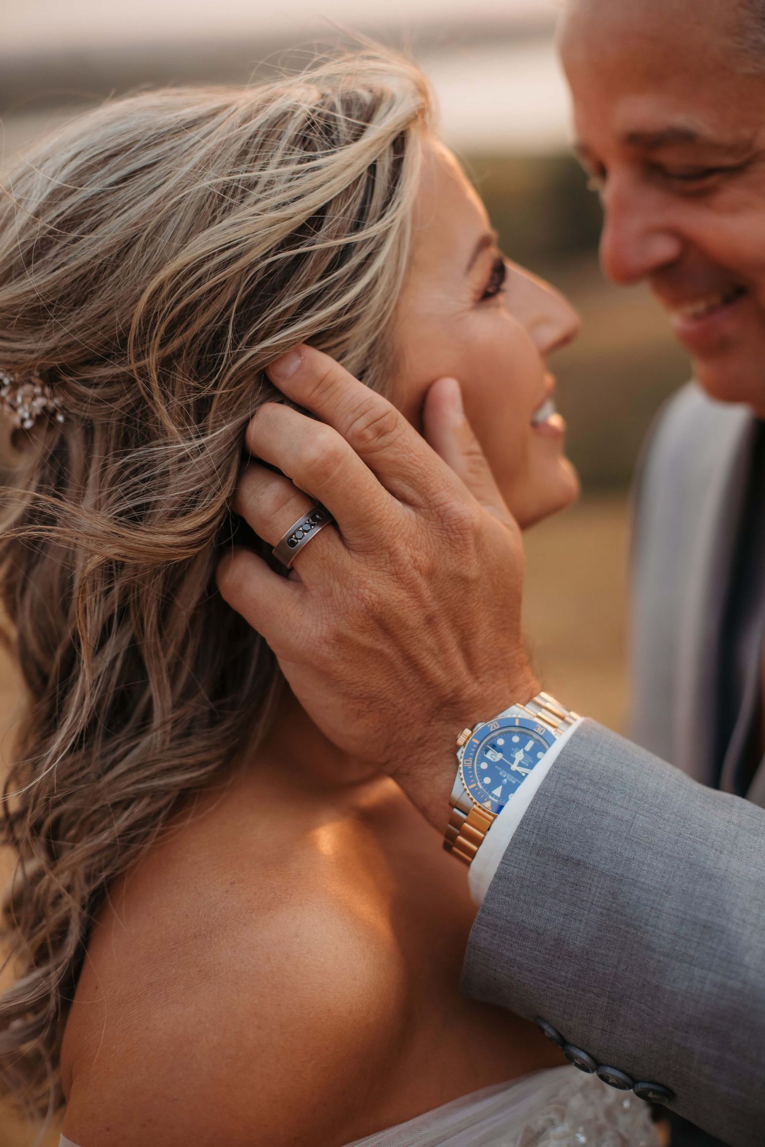 A close-up shot of an intimate moment between newlyweds showing a silver watch and wedding ring.