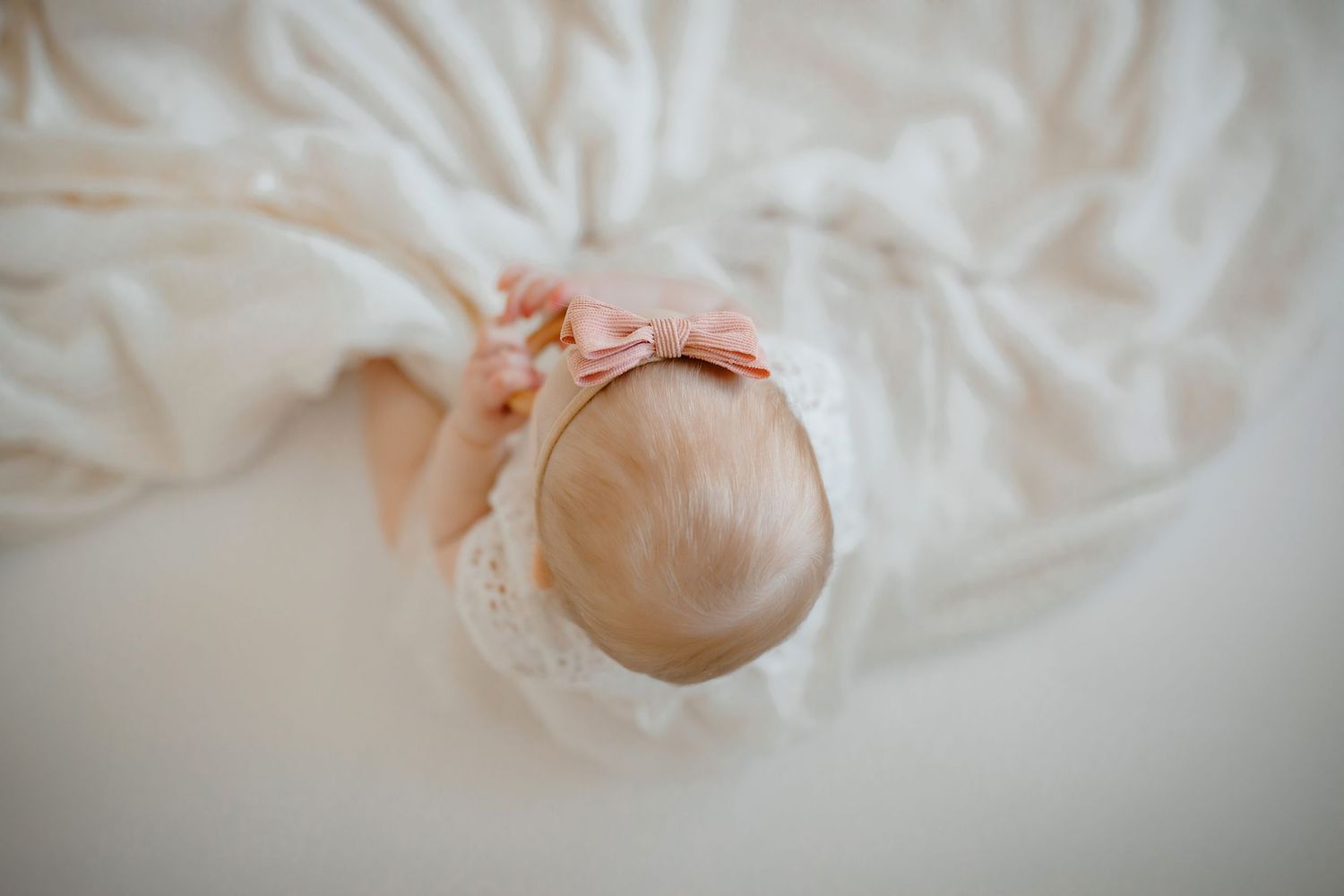 Overhead view of baby in white dress with pink bow on white background.