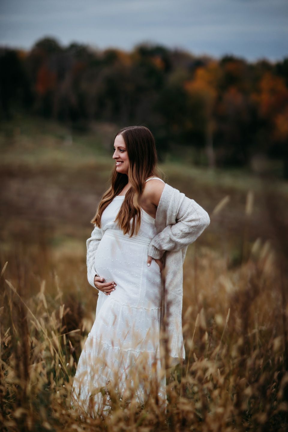 A feminine figure in a flowing white dress and cardigan stands in an autumn field with warm fall colors in the background.