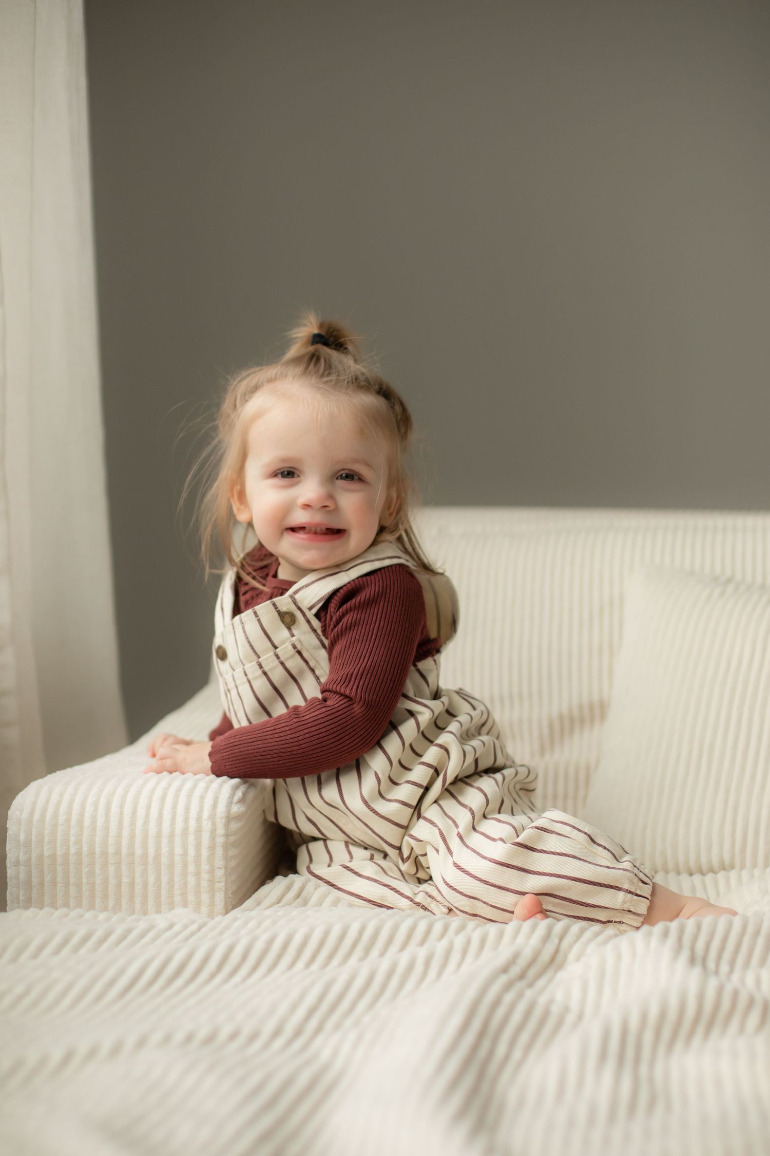 A sequence of images showing a small child rolling and playing on a white couch with striped pillows.