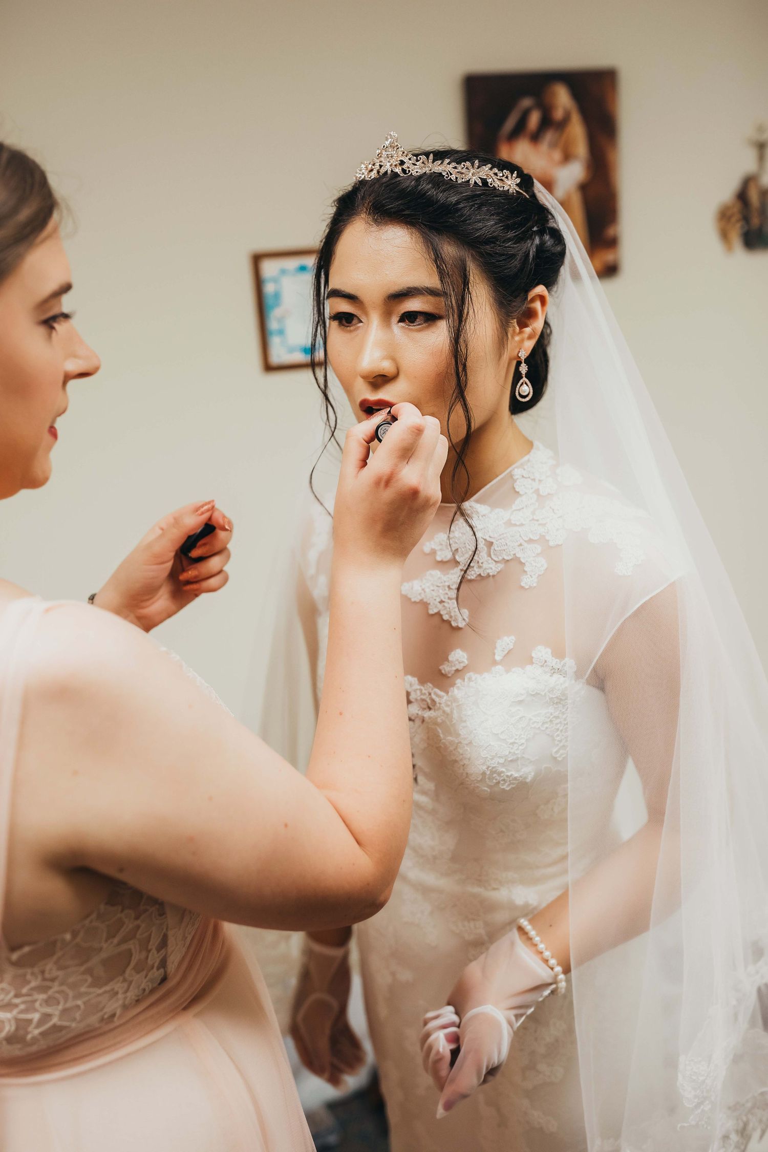 Wedding preparation scene with bride in white lace dress and veil getting final touches.