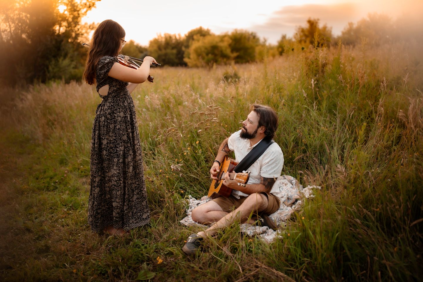 Couple shares an intimate moment with guitar in a golden meadow.