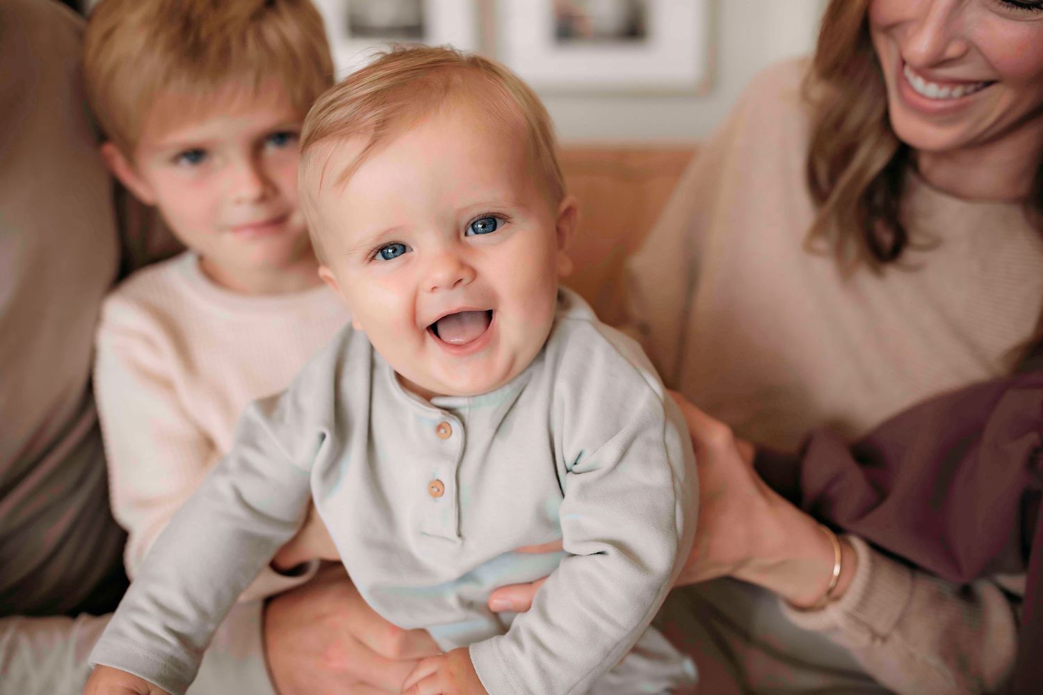 A baby sits on a couch laughing while surrounded by loved ones.