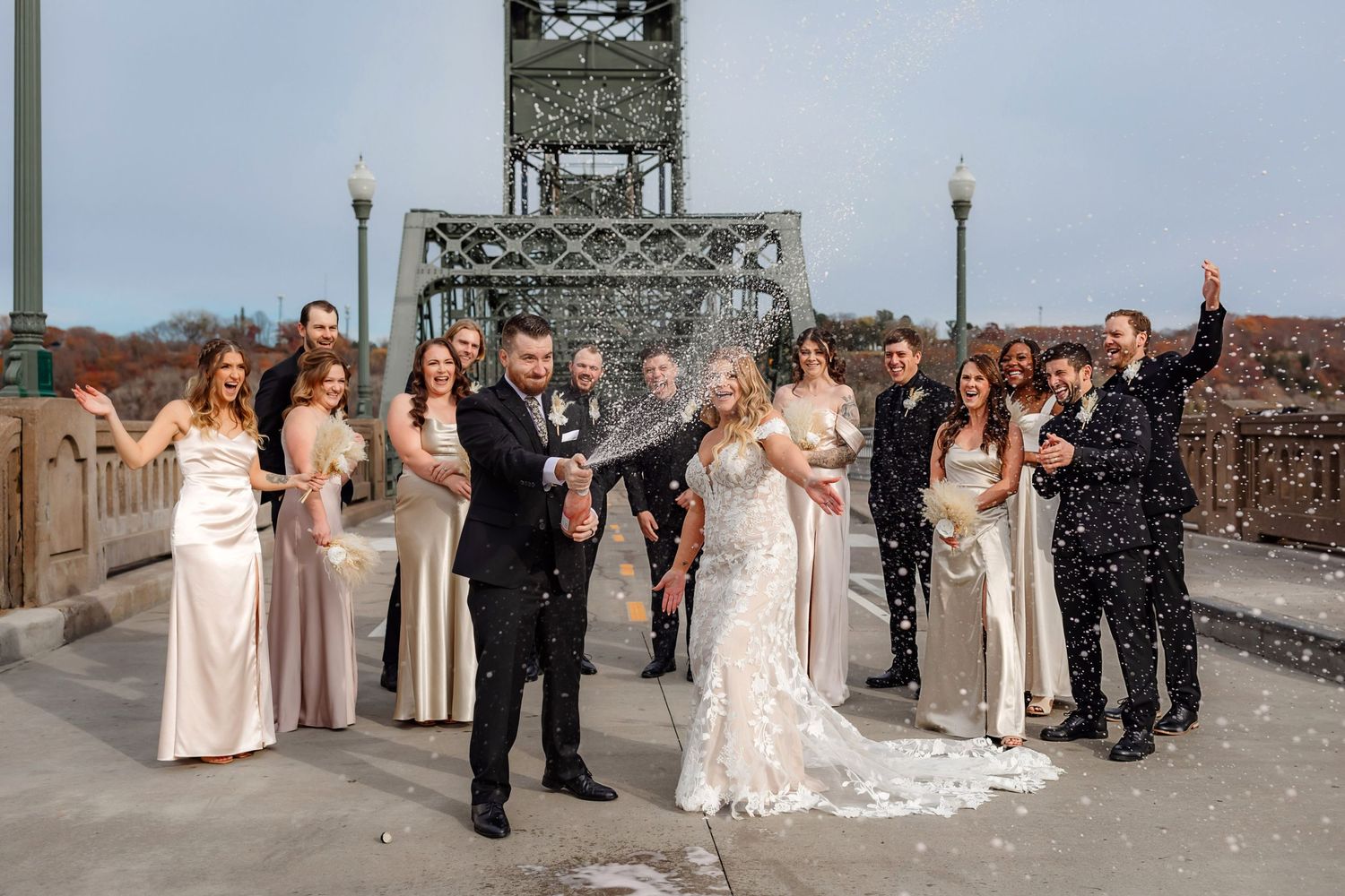 Wedding celebration group shot with confetti on industrial steel bridge.