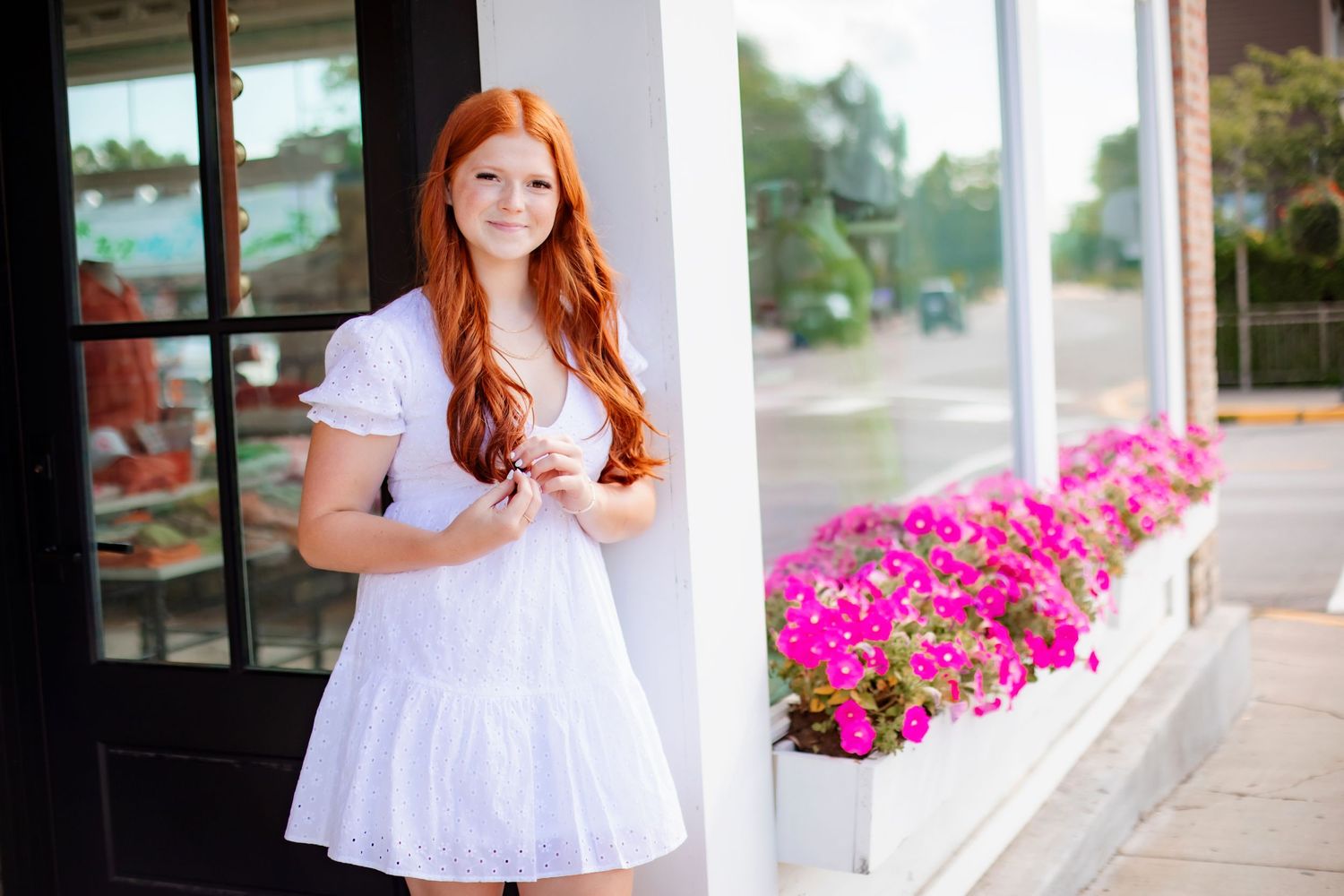 Portrait by storefront with white dress and pink flowers in window boxes.