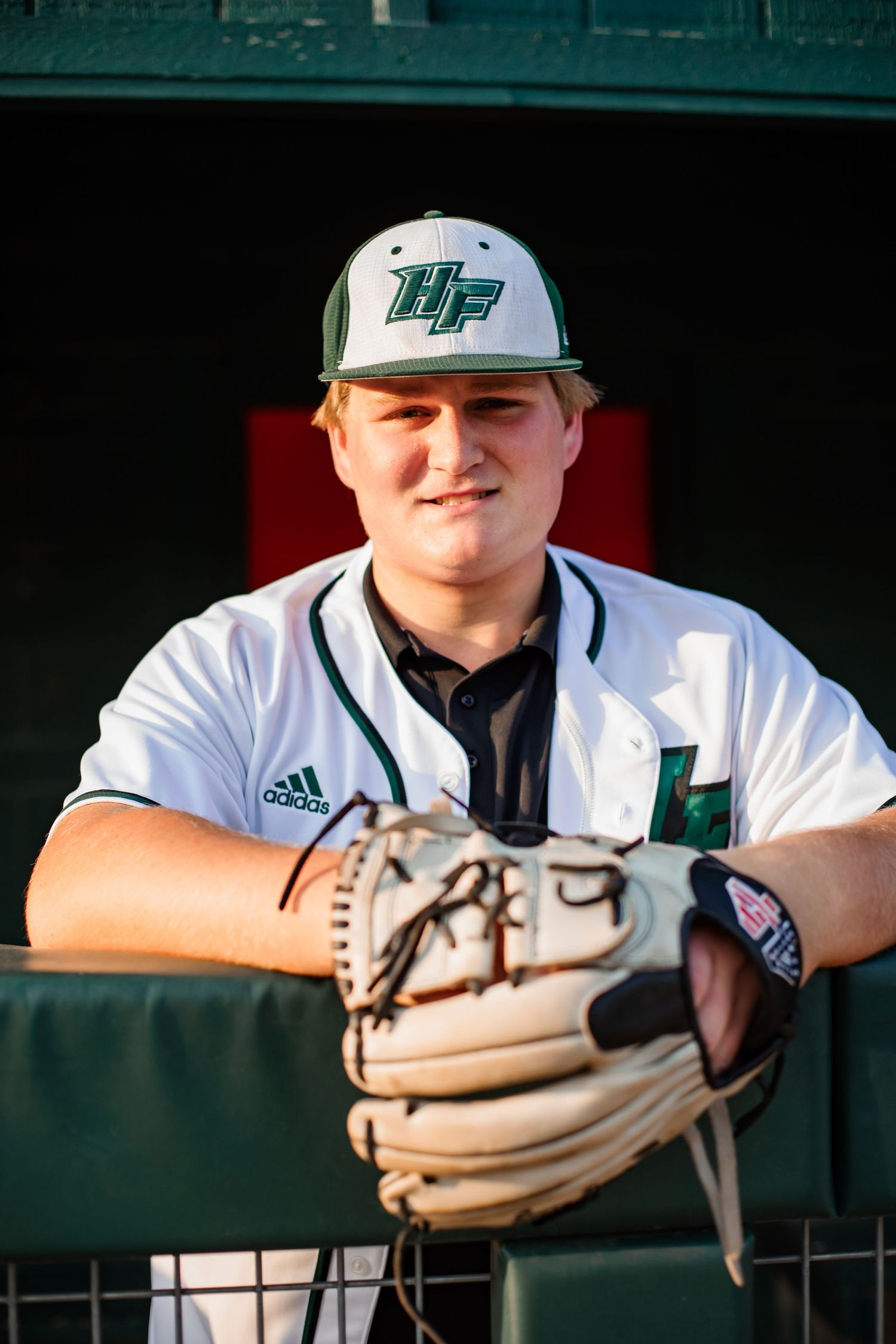 Baseball player in white uniform with cap and glove posing in dugout.