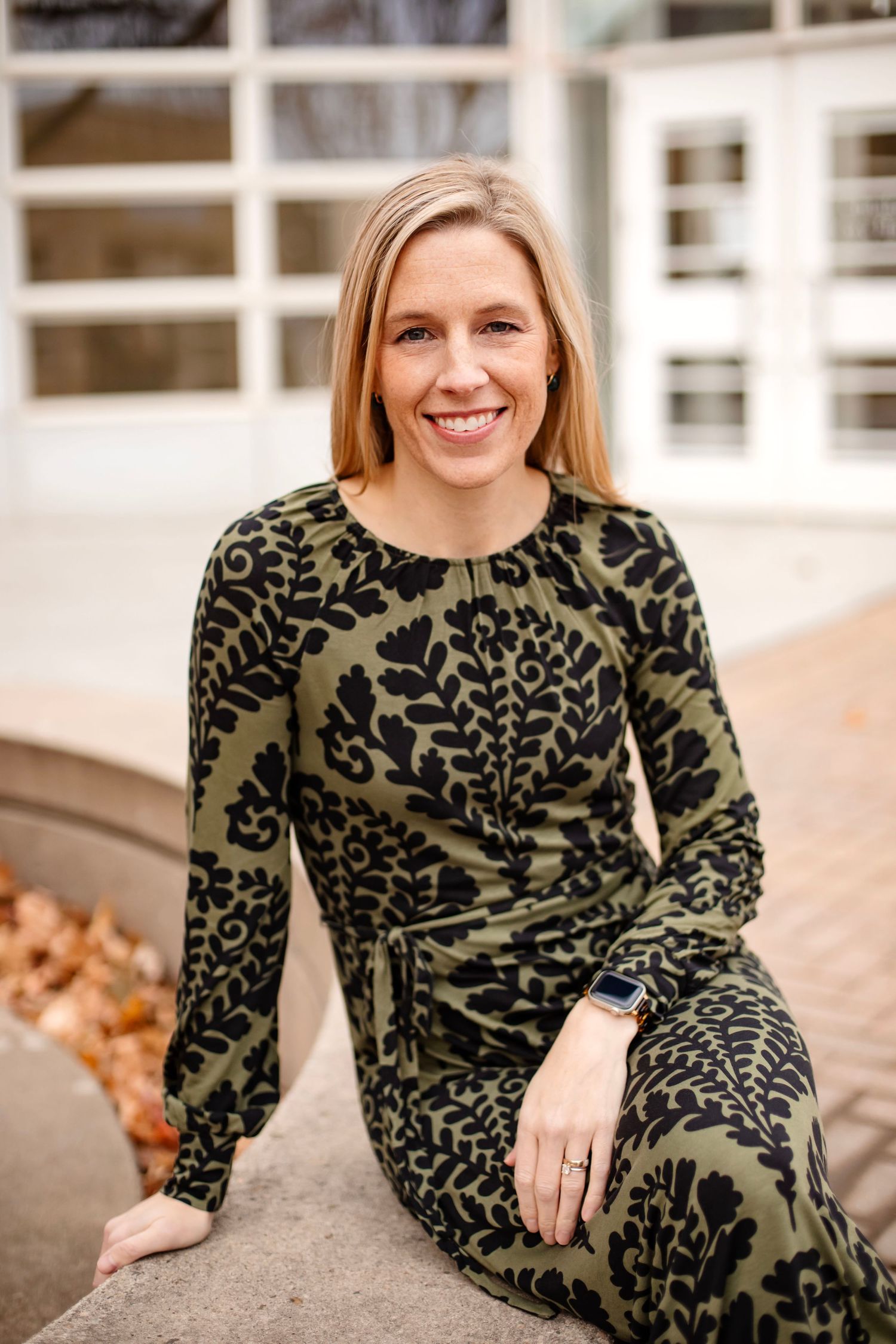 Casual portrait in green and black patterned dress sitting outdoors.