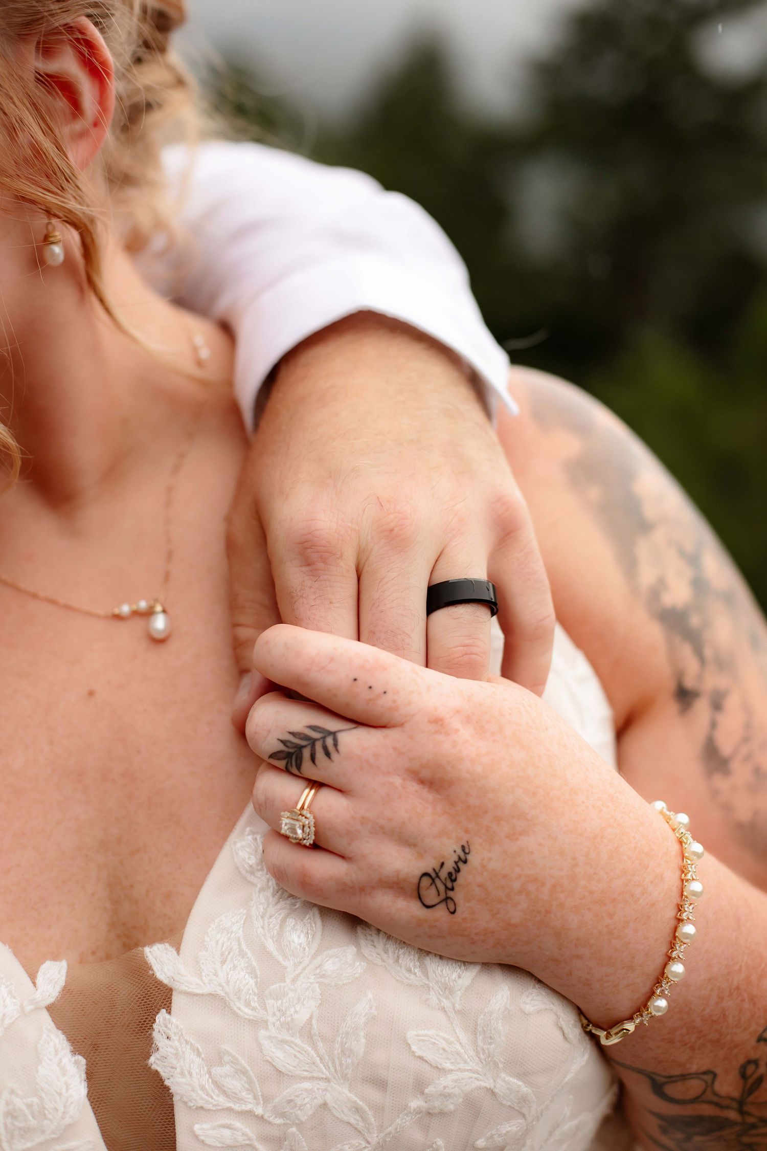 Close-up shots of hands wearing wedding rings and tattoos against white lace dress fabric.