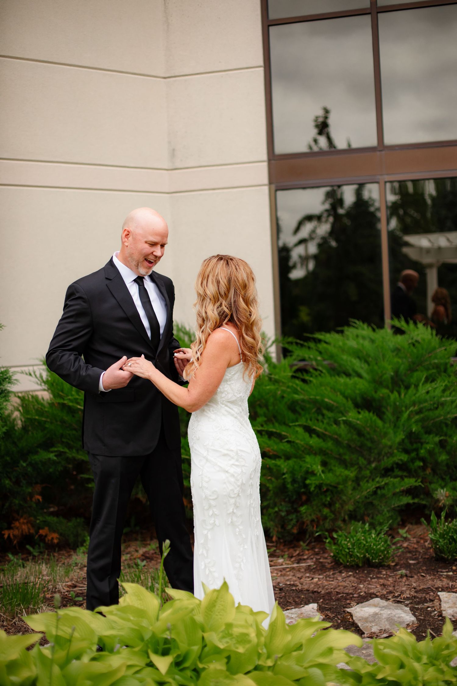 A couple dances together outdoors near lush greenery and a building exterior.