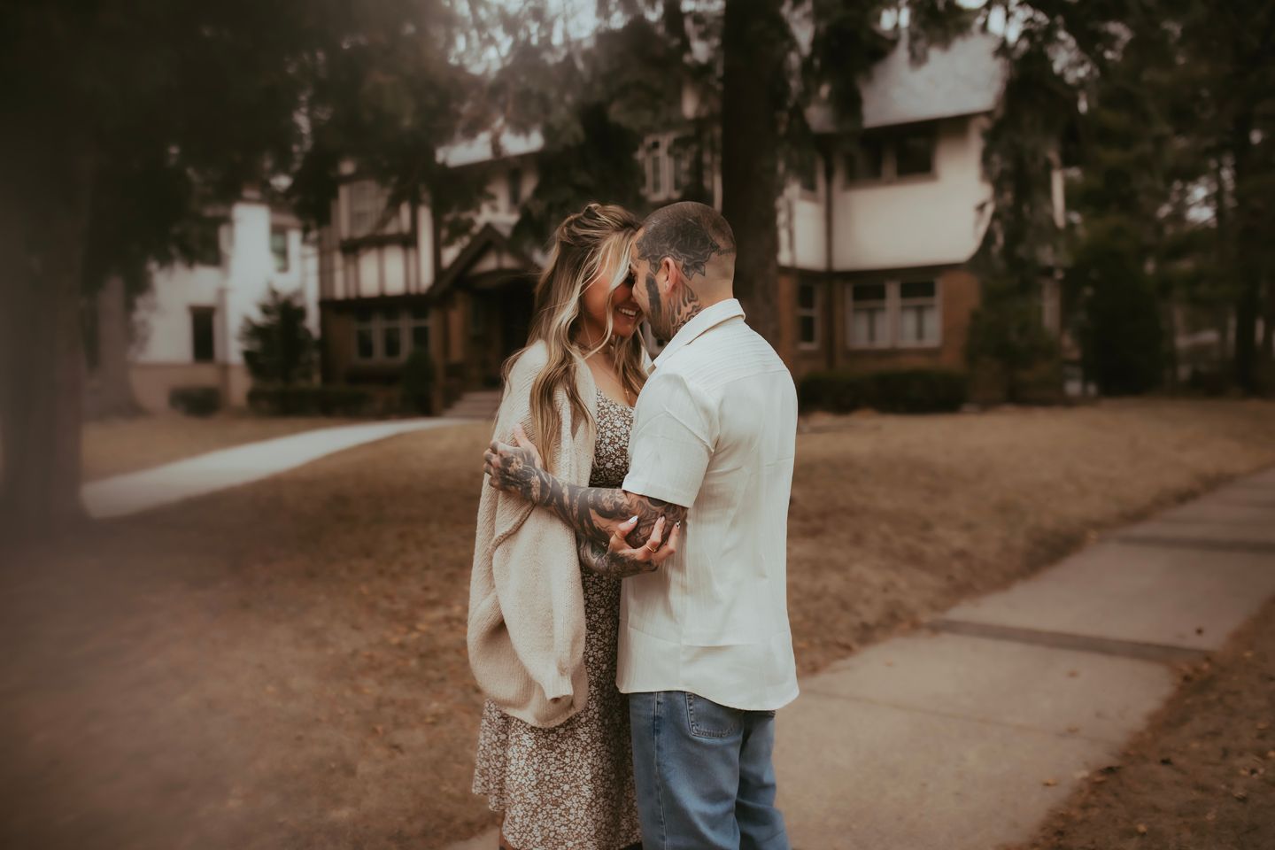 A couple stands together in an autumn setting during a romantic engagement photoshoot at sunset.