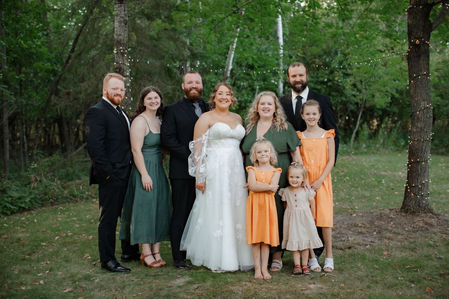 Wedding group photo with family members in teal and orange dresses against a forest backdrop.