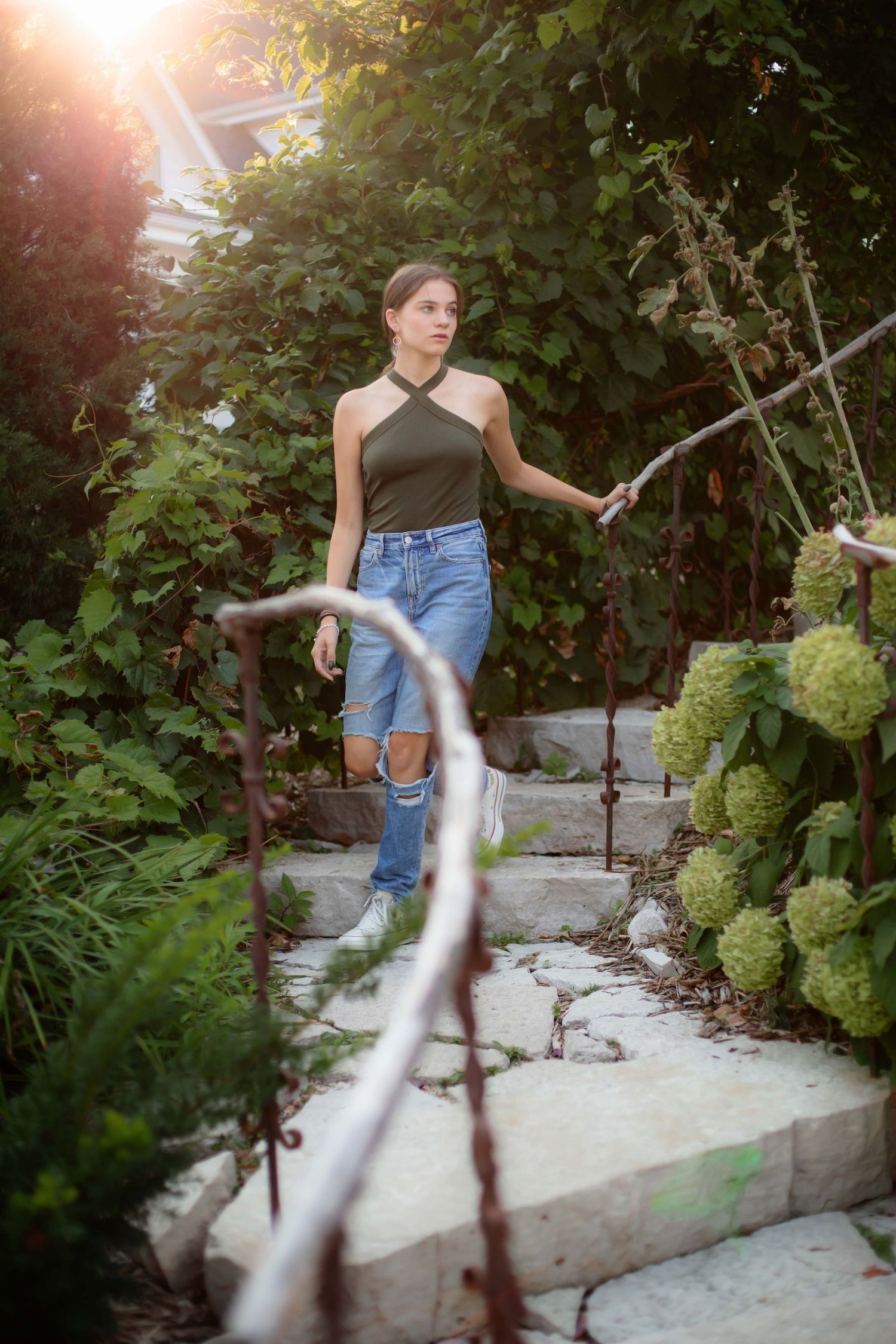 A casual summer outfit with high-waisted jeans and black top posed on garden steps at golden hour.
