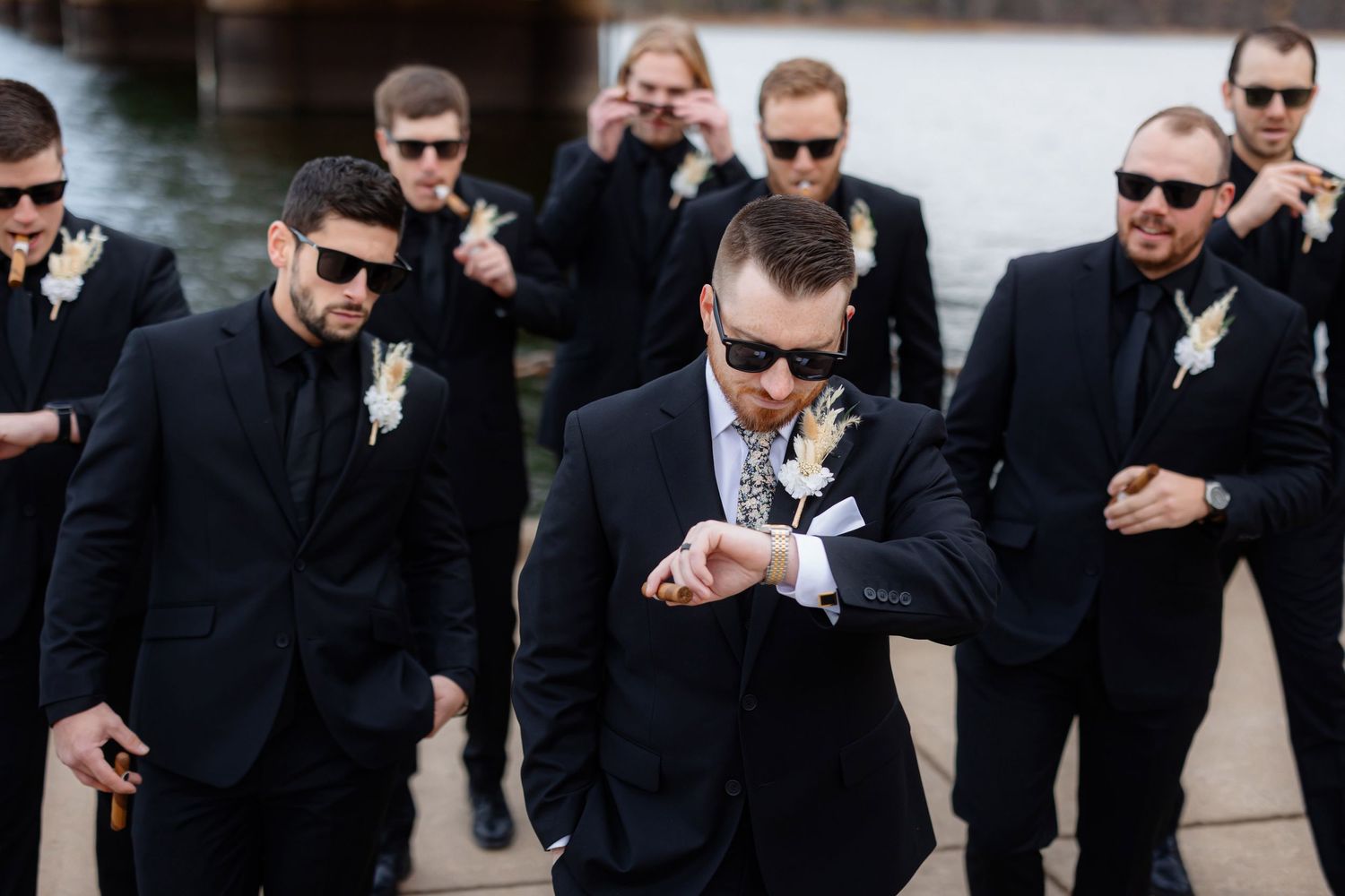 Groomsmen in matching black suits check their watches in synchronized fashion.